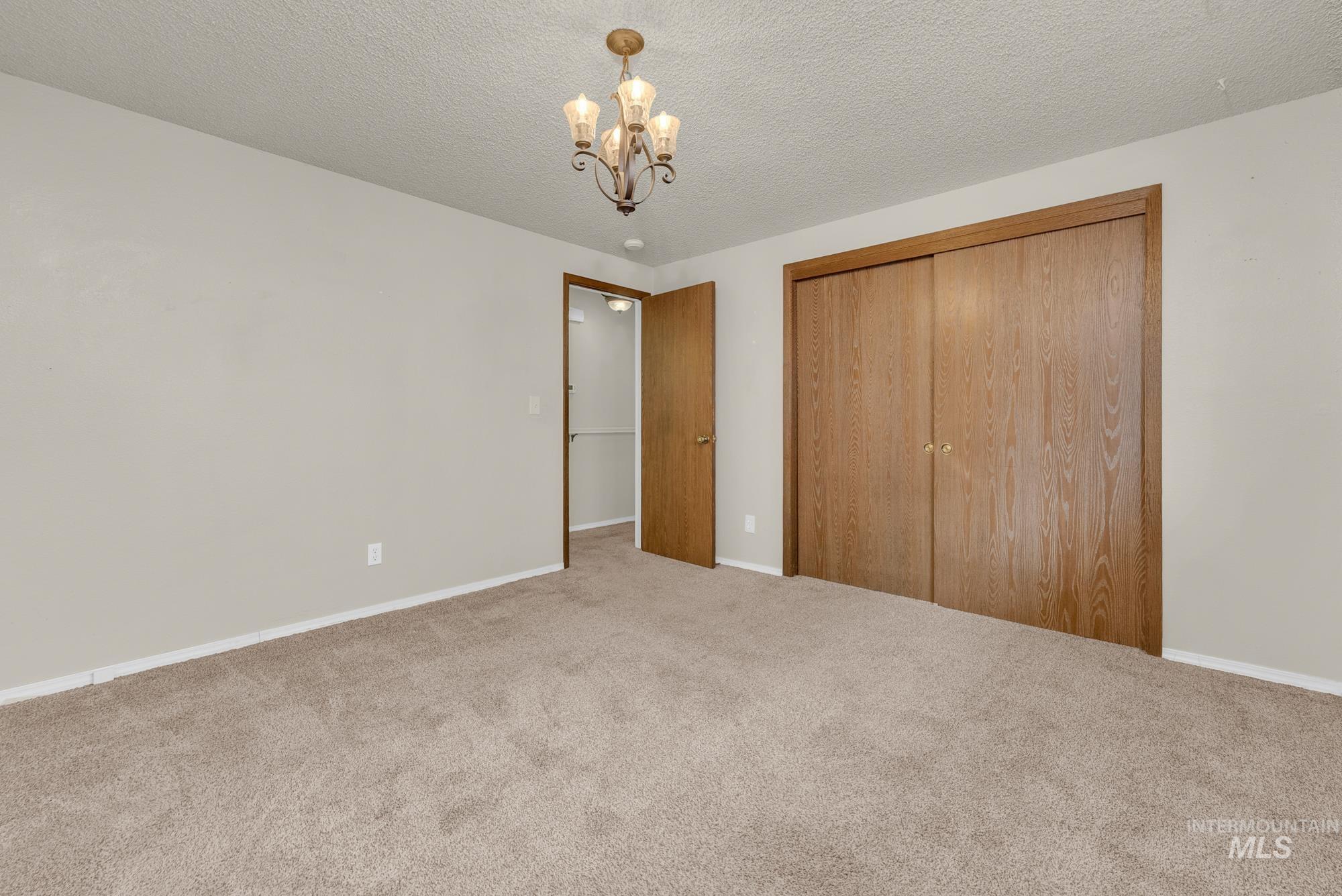 Unfurnished bedroom featuring a textured ceiling, carpet flooring, a chandelier, and a closet