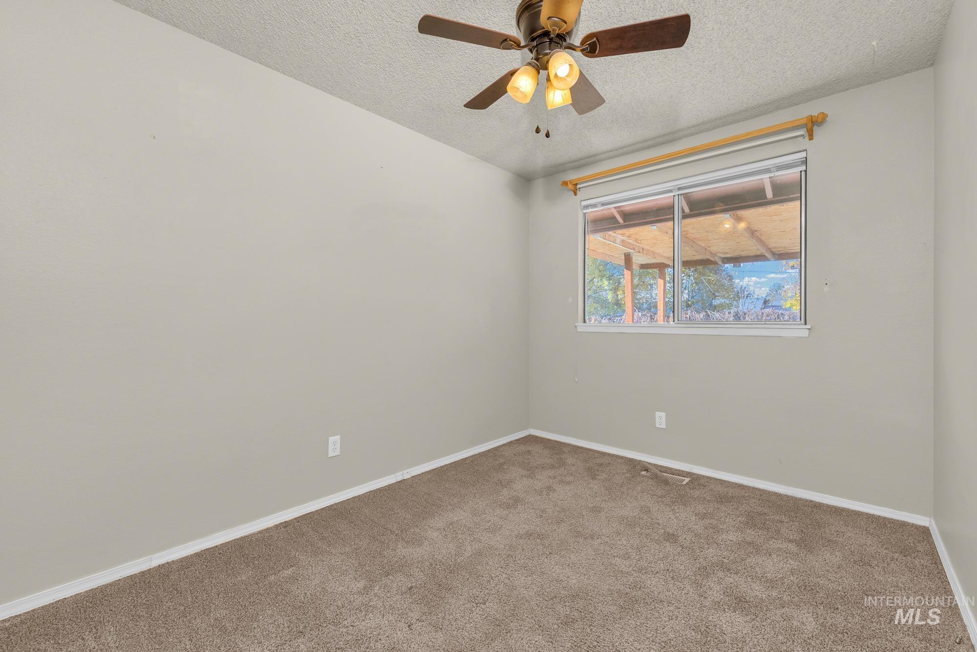 Empty room featuring carpet flooring, a textured ceiling, and a ceiling fan