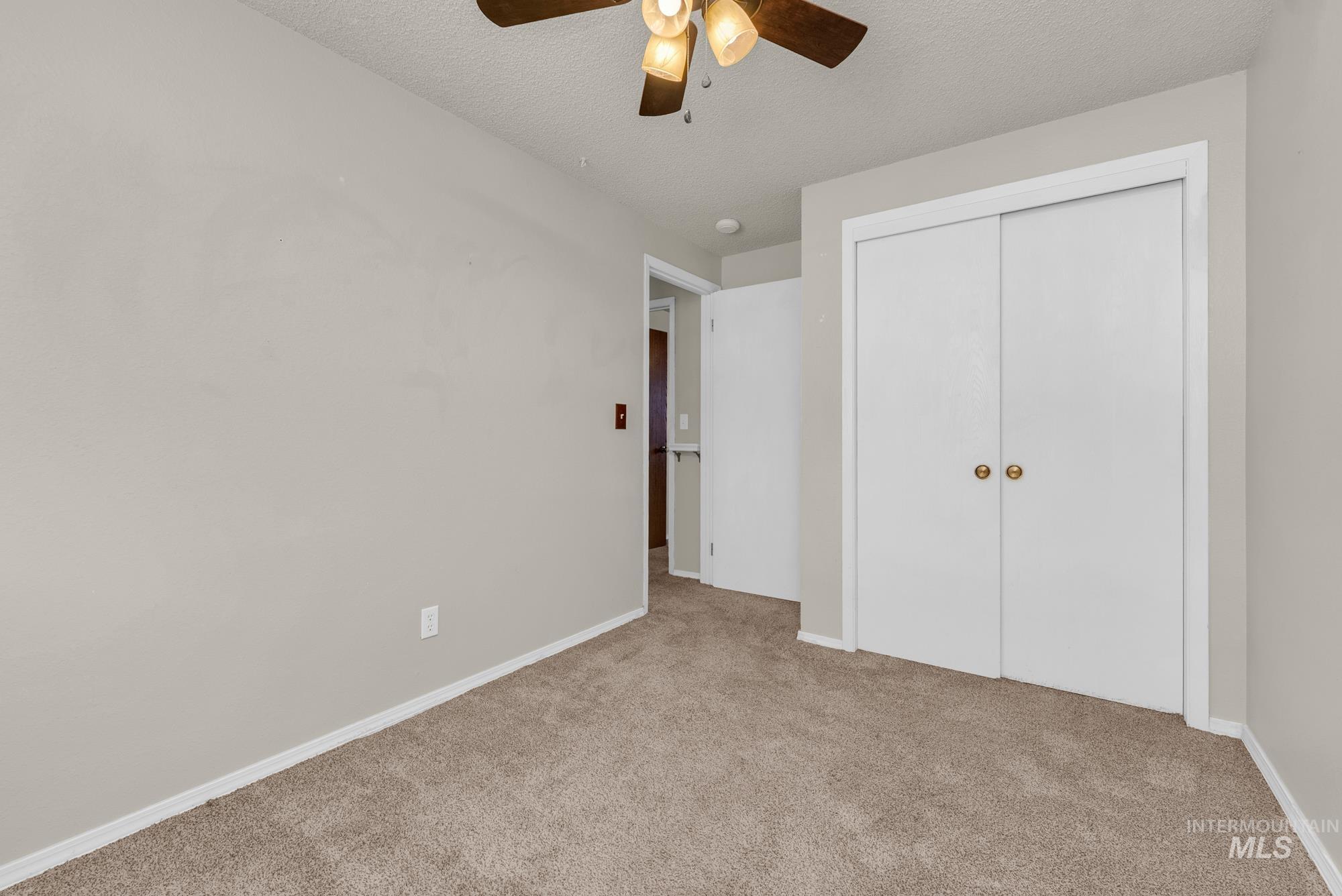Unfurnished bedroom with carpet, a textured ceiling, a closet, and a ceiling fan