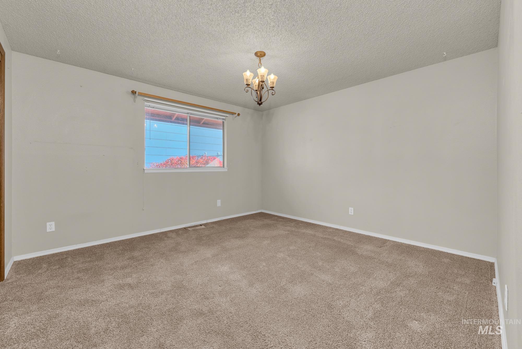 Empty room with a textured ceiling, carpet, and a chandelier