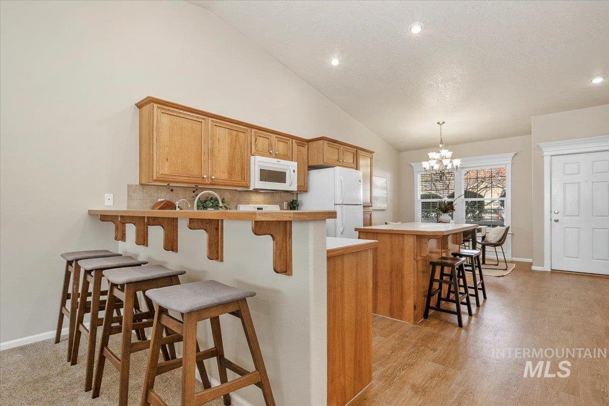 Kitchen with a breakfast bar, a peninsula, decorative backsplash, light countertops, and white appliances