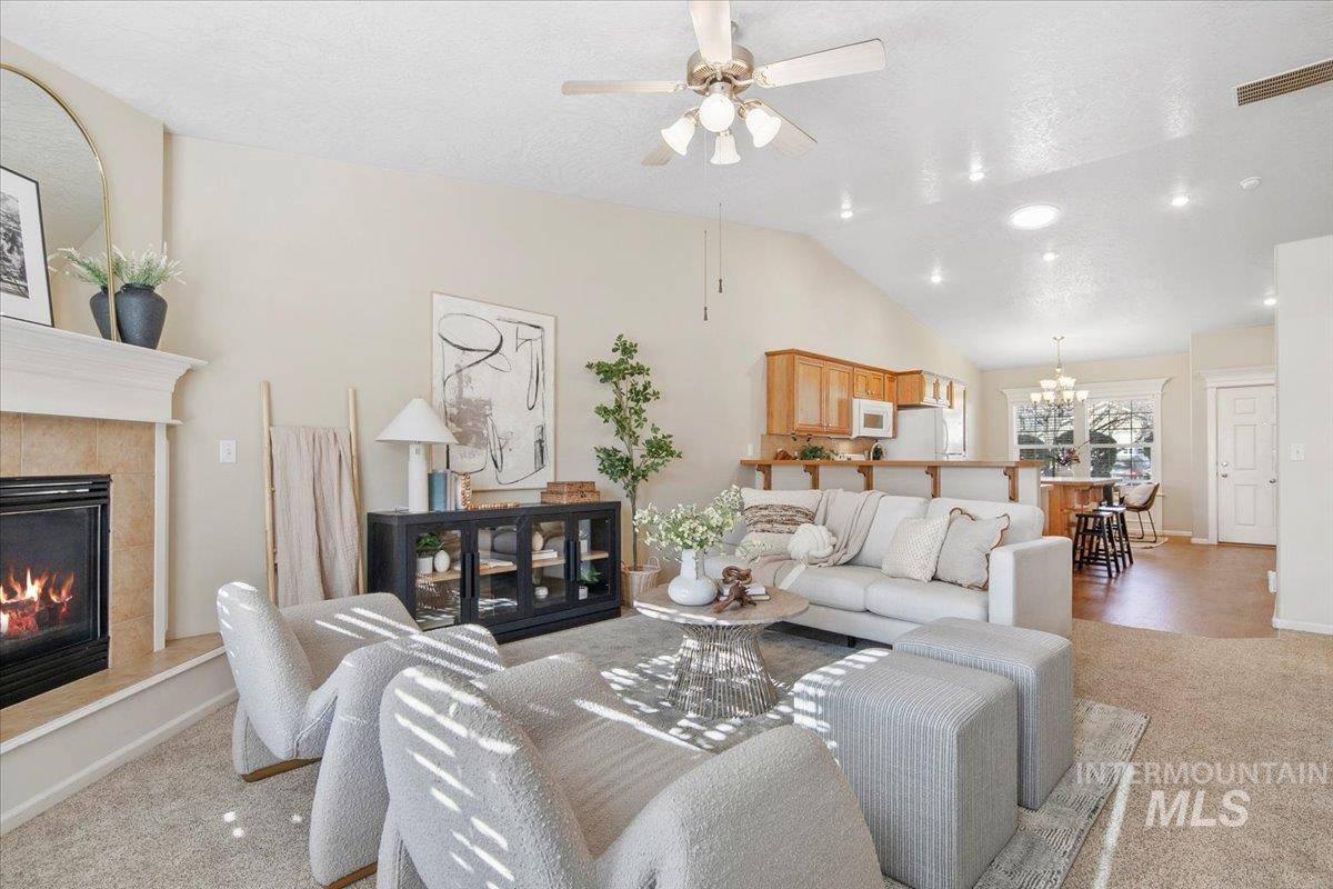Living area featuring light carpet, a fireplace, a chandelier, vaulted ceiling, and a ceiling fan