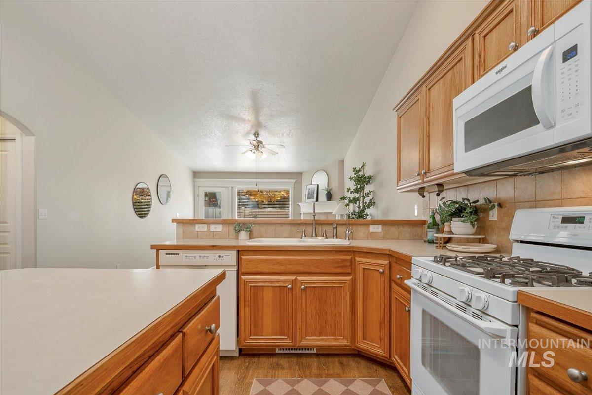 Kitchen with white appliances, light countertops, brown cabinets, decorative backsplash, and a textured ceiling