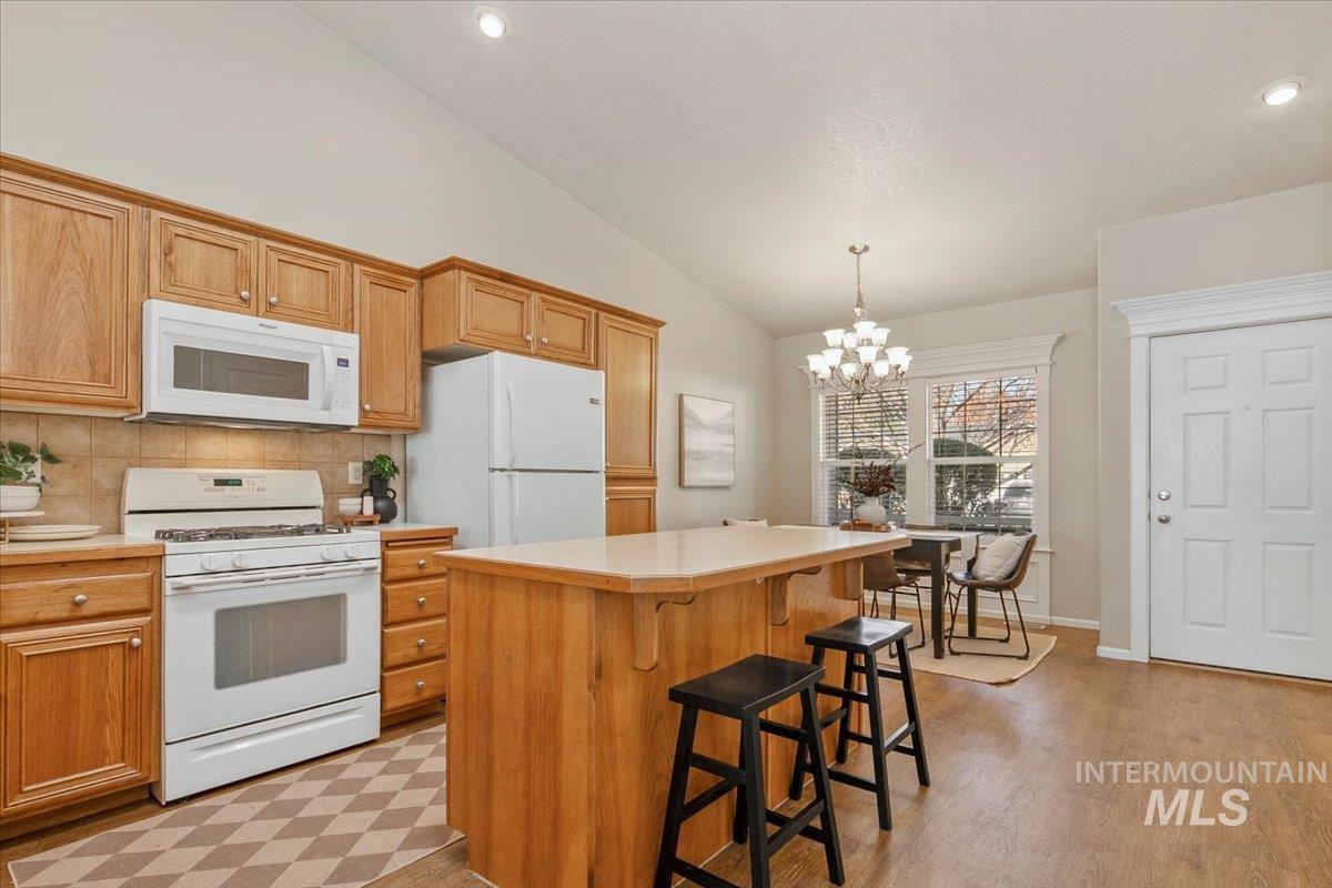 Kitchen featuring white appliances, light countertops, lofted ceiling, a kitchen bar, and tasteful backsplash