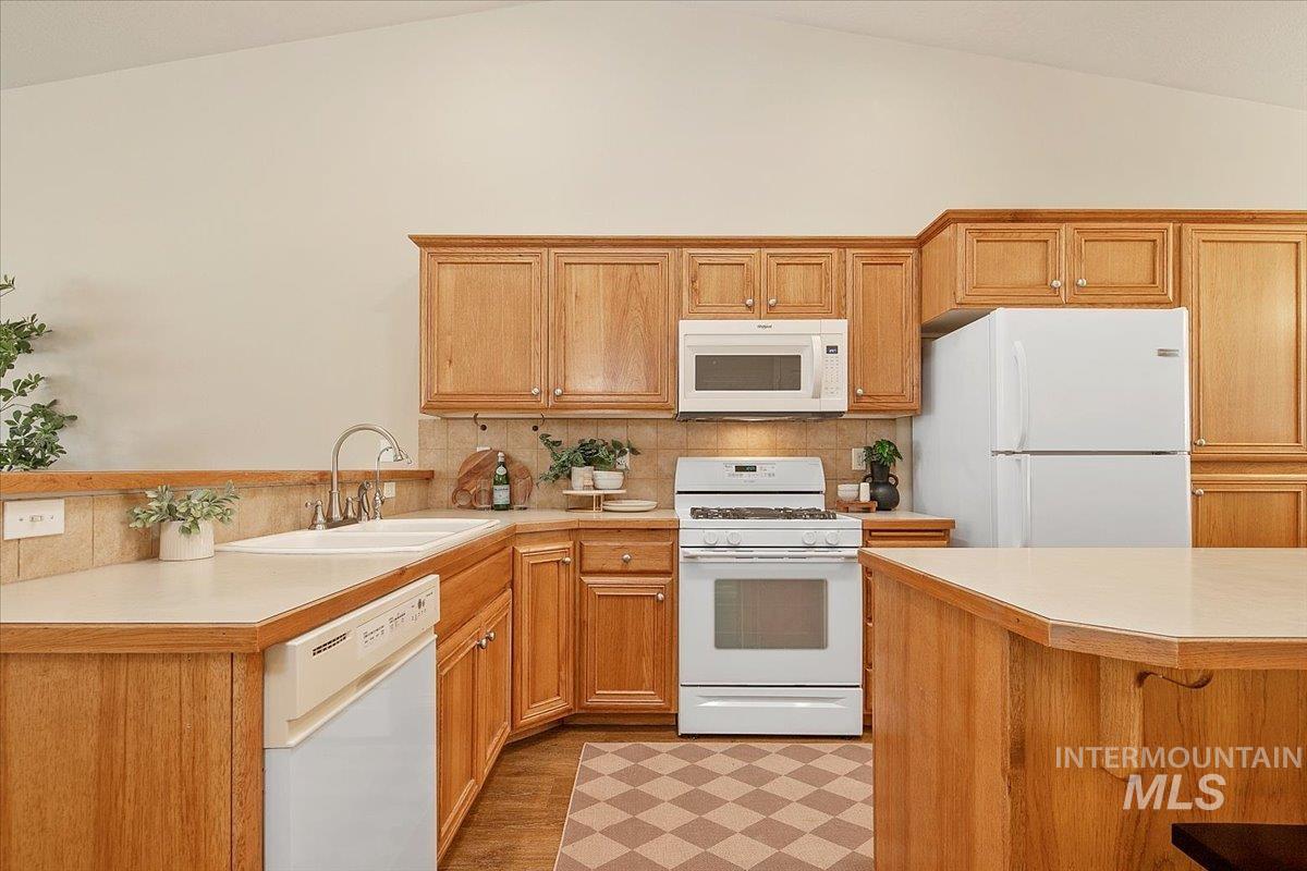 Kitchen featuring white appliances, light countertops, a kitchen bar, backsplash, and a peninsula