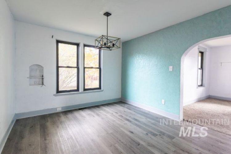 Empty room with arched walkways, a chandelier, and light wood-style floors