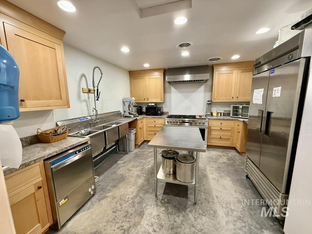 Kitchen with light brown cabinets, high end appliances, recessed lighting, concrete floors, and wall chimney range hood