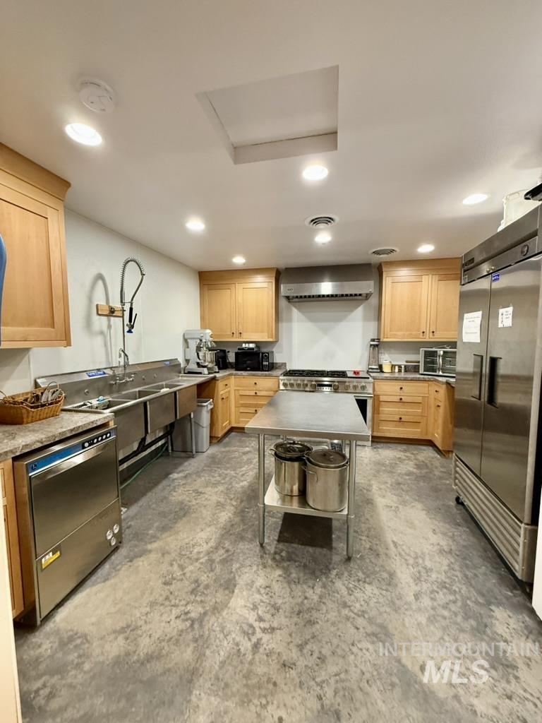 Kitchen with light brown cabinetry, premium appliances, unfinished concrete floors, recessed lighting, and wall chimney range hood