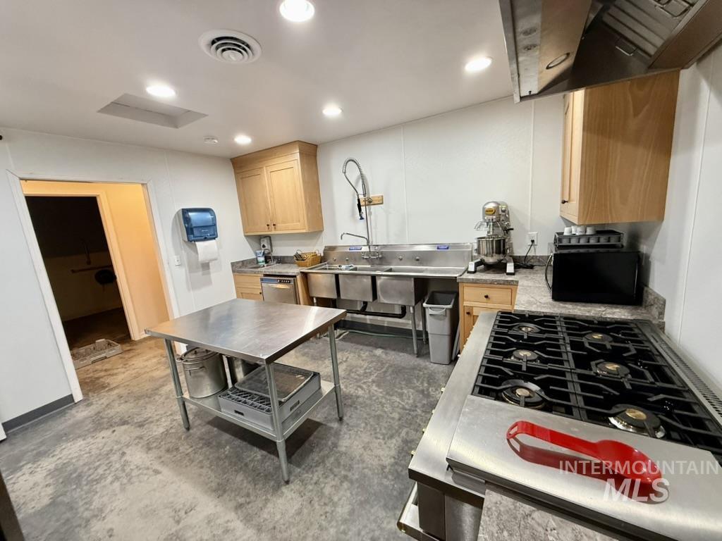 Kitchen with light brown cabinets, extractor fan, light countertops, black microwave, and recessed lighting