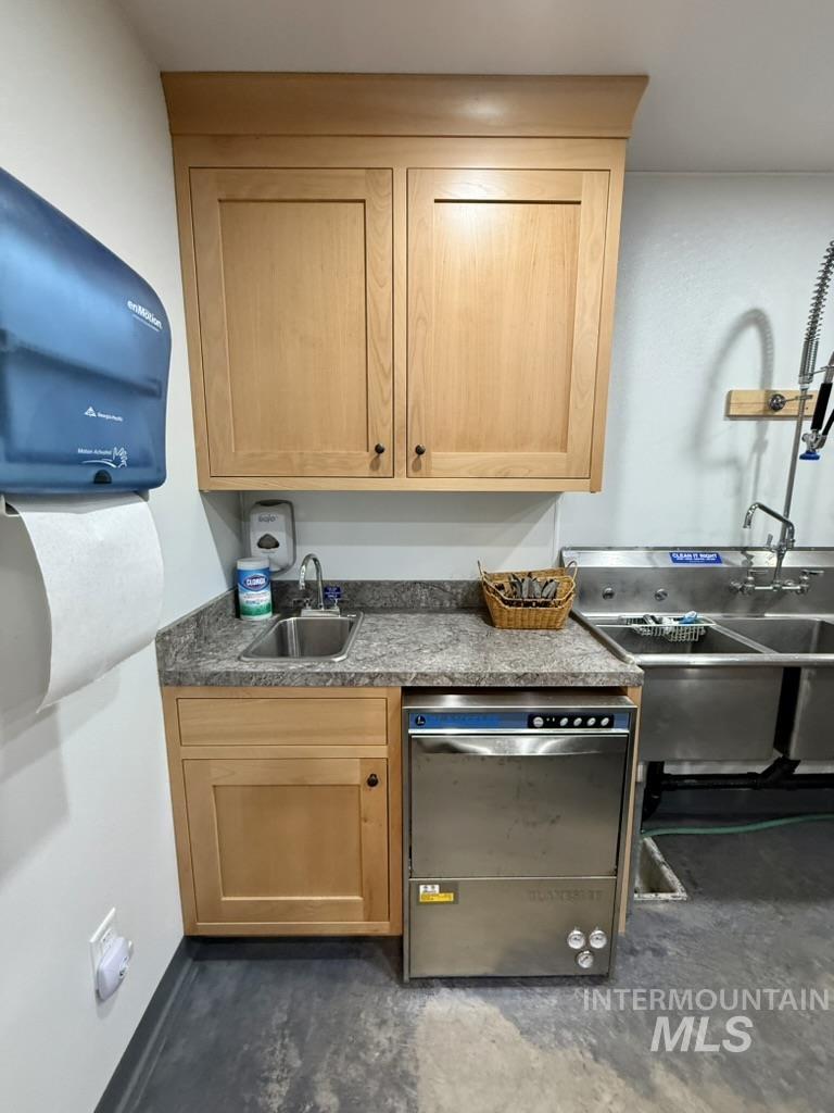 Kitchen with dishwasher, dark countertops, light brown cabinets, and concrete floors