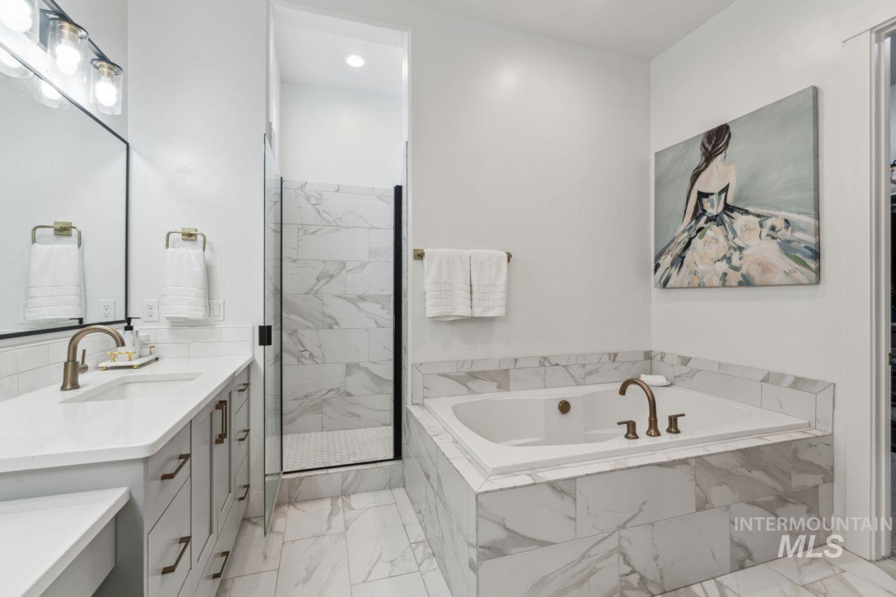 Full bath featuring vanity, marble look tiles, a marble finish shower, and a garden tub