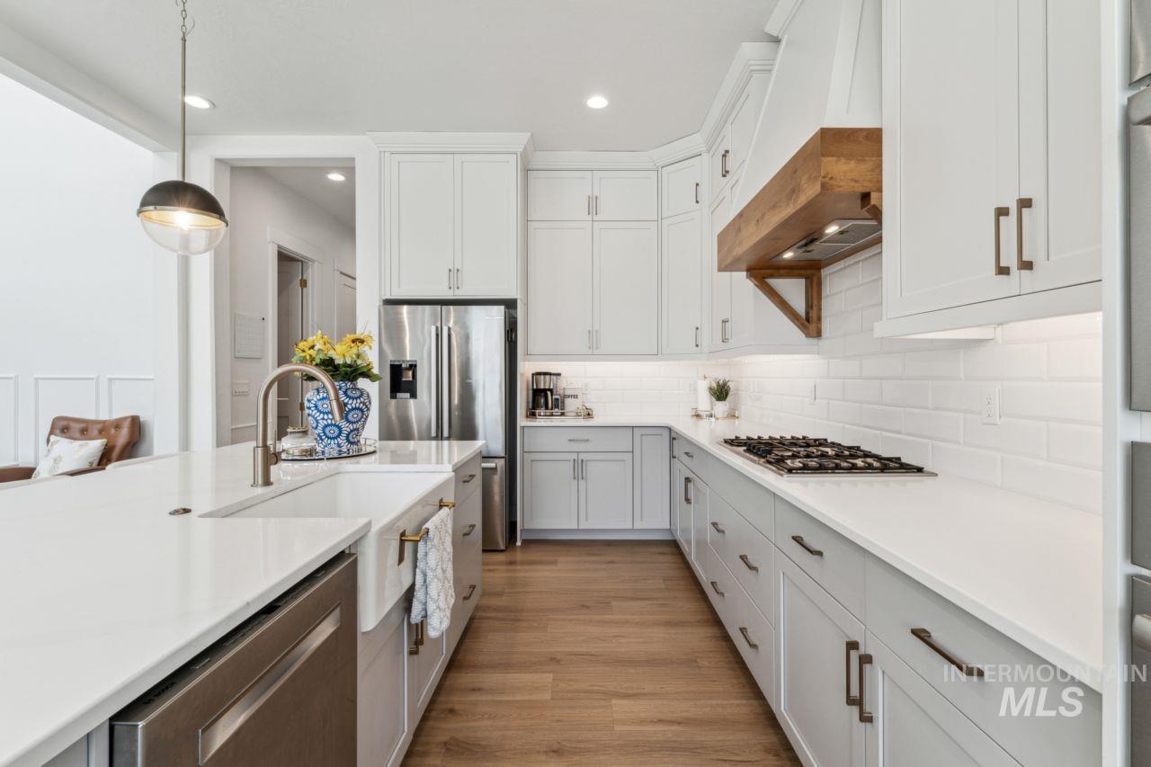 Kitchen featuring stainless steel appliances, tasteful backsplash, light countertops, light wood-style flooring, and pendant lighting