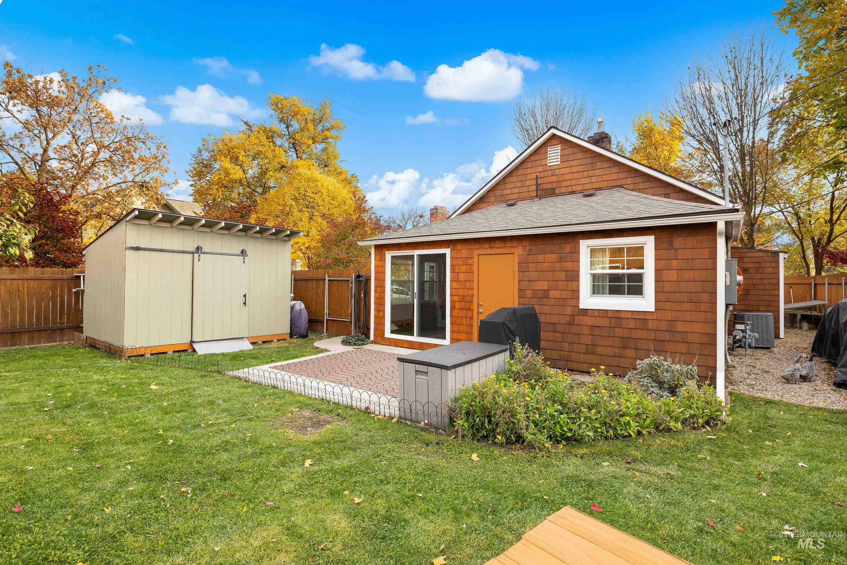 Back of house with a storage shed, a fenced backyard, a patio area, roof with shingles, and a chimney