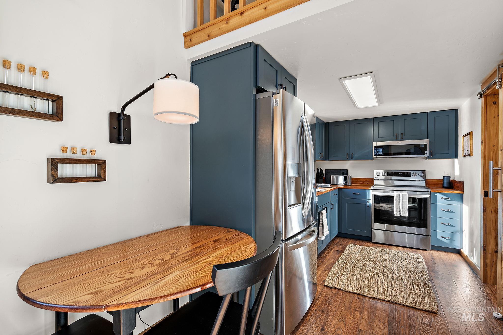 Kitchen featuring appliances with stainless steel finishes, blue cabinets, and dark wood-type flooring