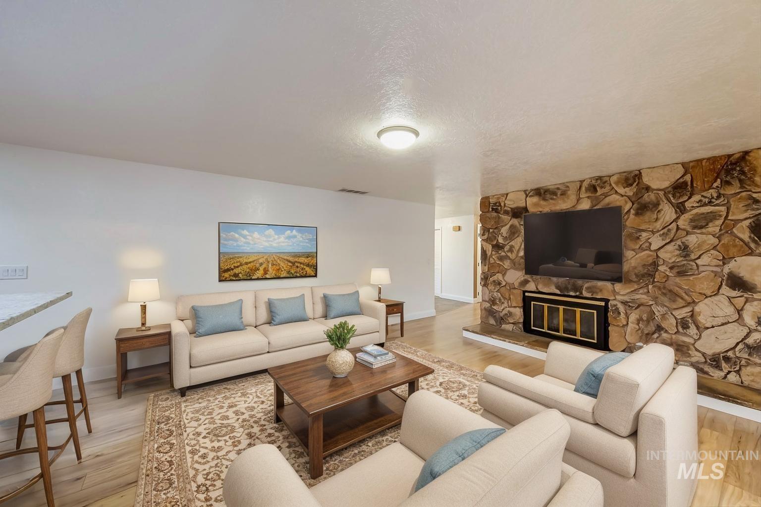 Living room featuring a stone fireplace, light wood finished floors, and a textured ceiling