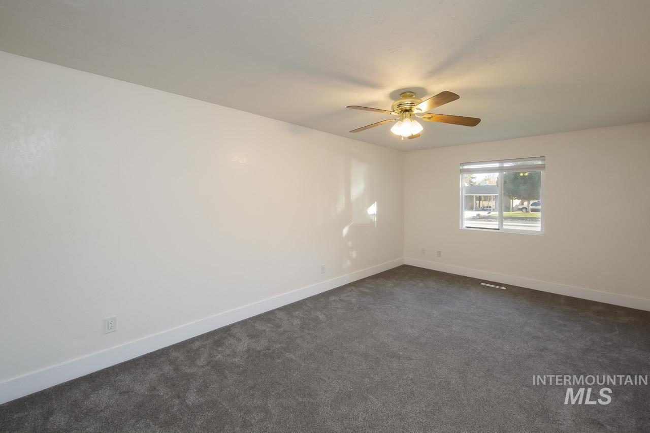 Empty room with dark colored carpet and a ceiling fan