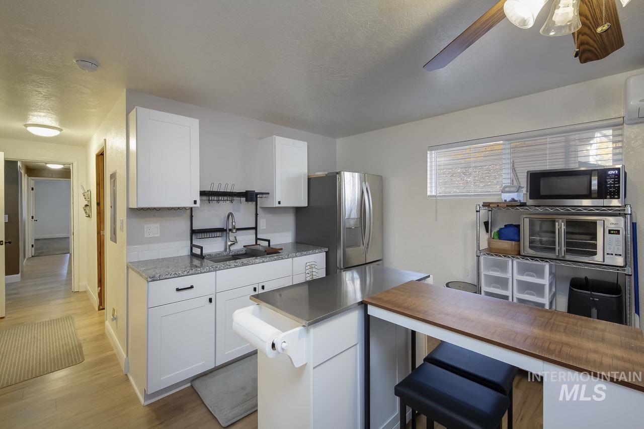 Kitchen featuring white cabinets, butcher block counters, appliances with stainless steel finishes, light wood-style floors, and a kitchen bar