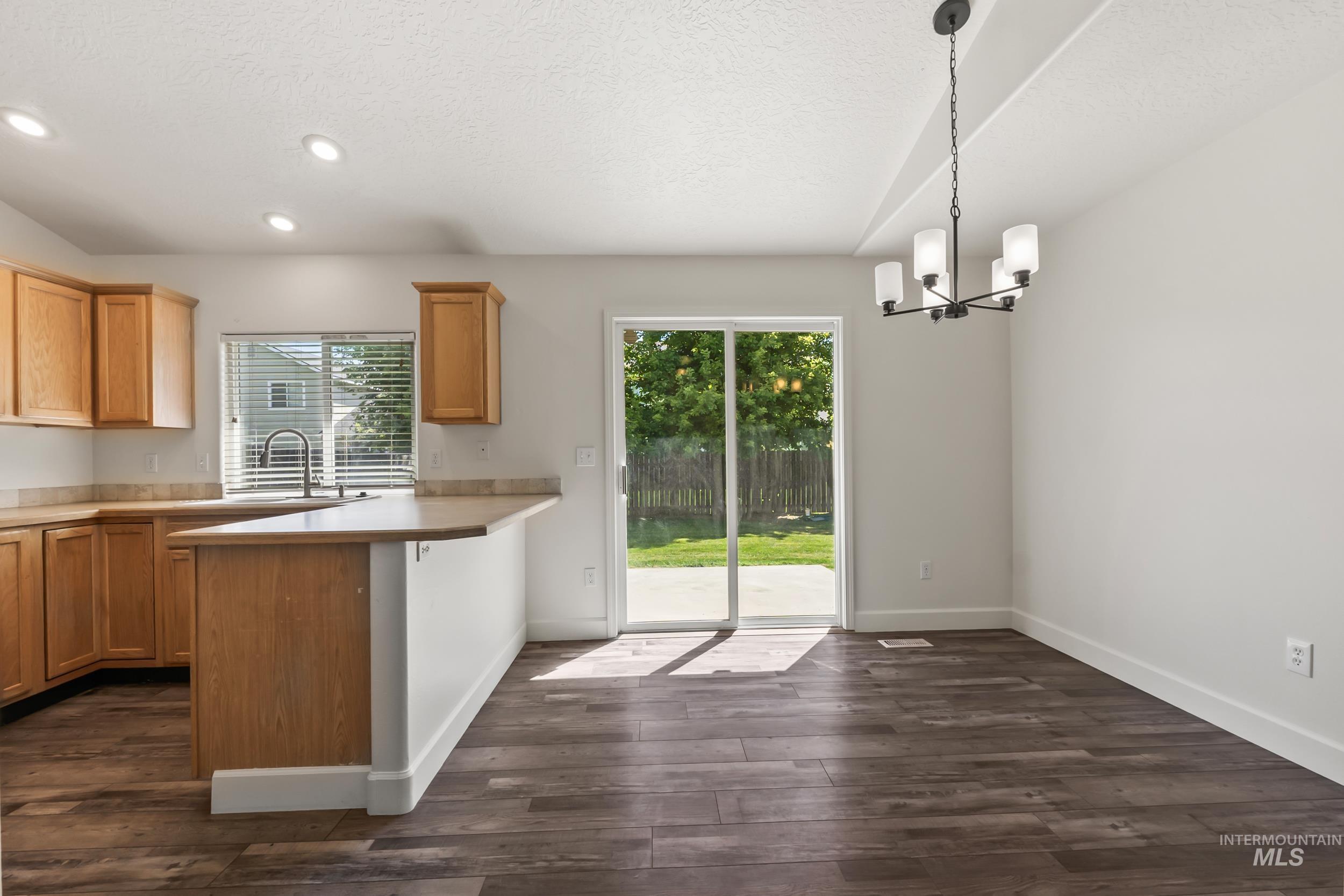 Kitchen featuring light countertops, a peninsula, a chandelier, pendant lighting, and dark wood-type flooring