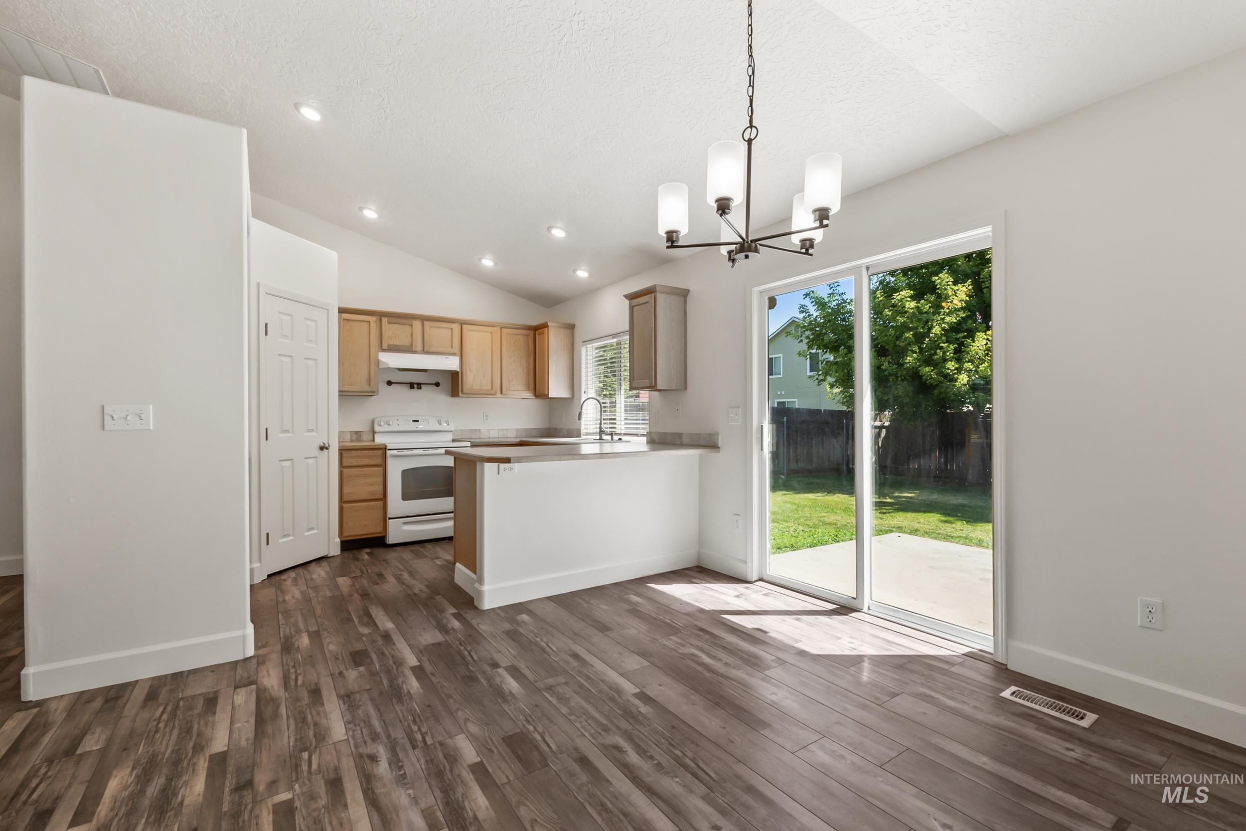 Kitchen featuring hanging light fixtures, electric range, a chandelier, vaulted ceiling, and light countertops