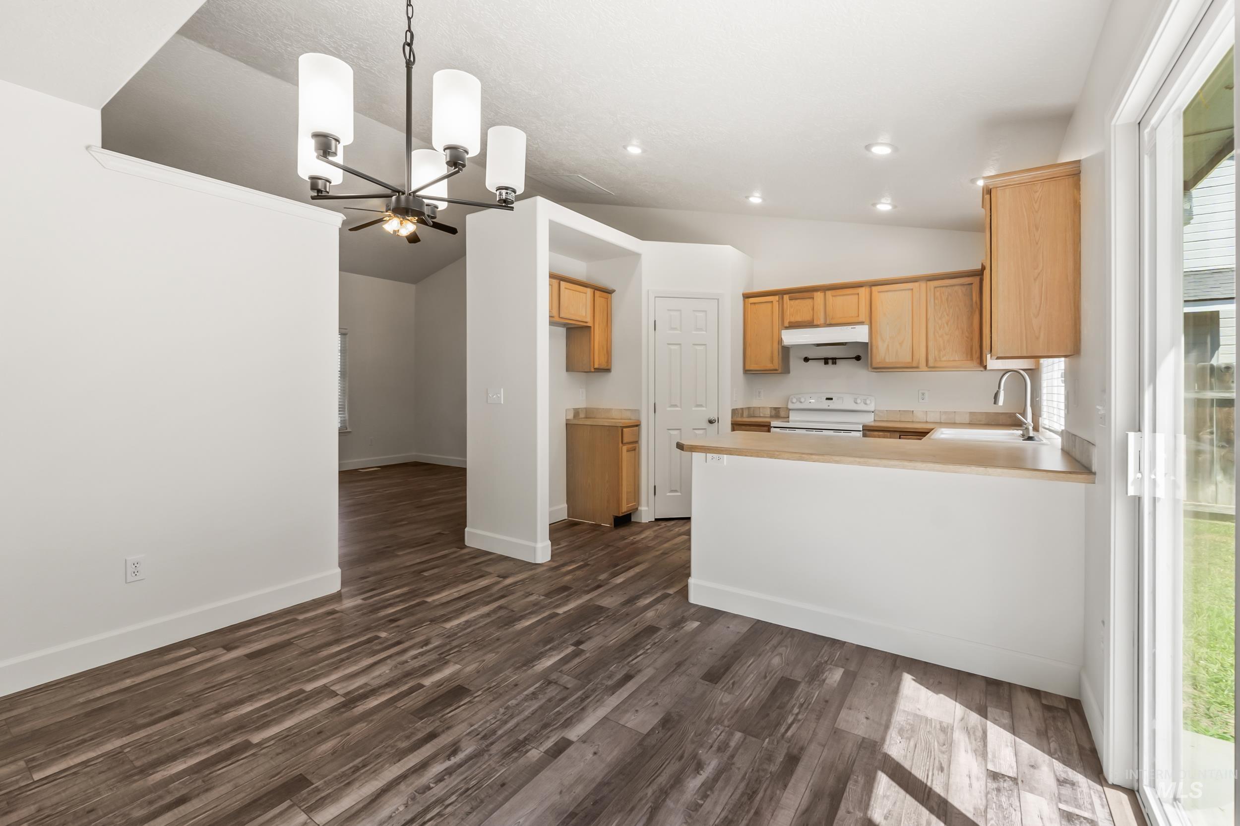Kitchen featuring vaulted ceiling, a chandelier, a peninsula, pendant lighting, and dark wood finished floors