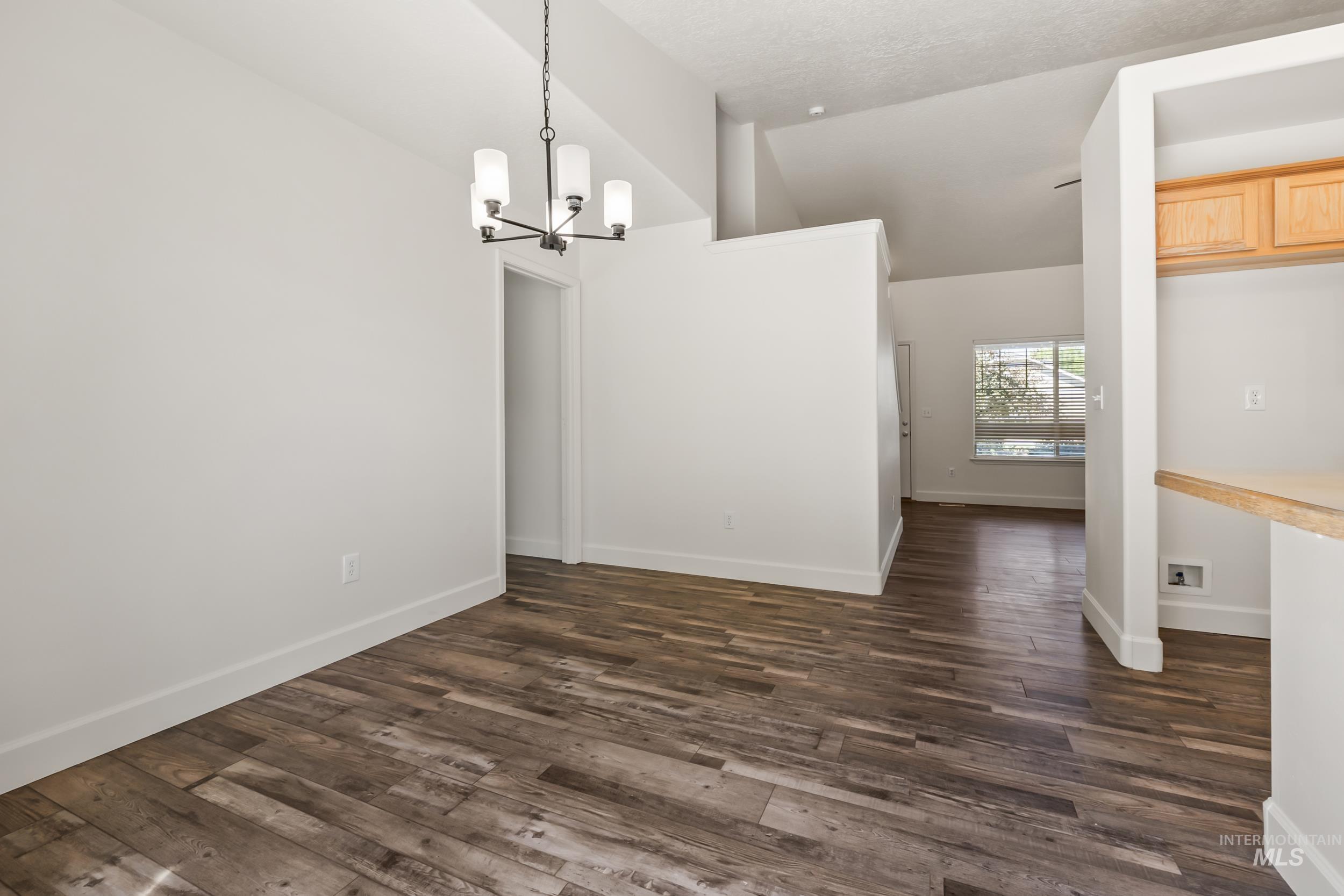 Unfurnished dining area featuring lofted ceiling, a chandelier, and dark wood-type flooring