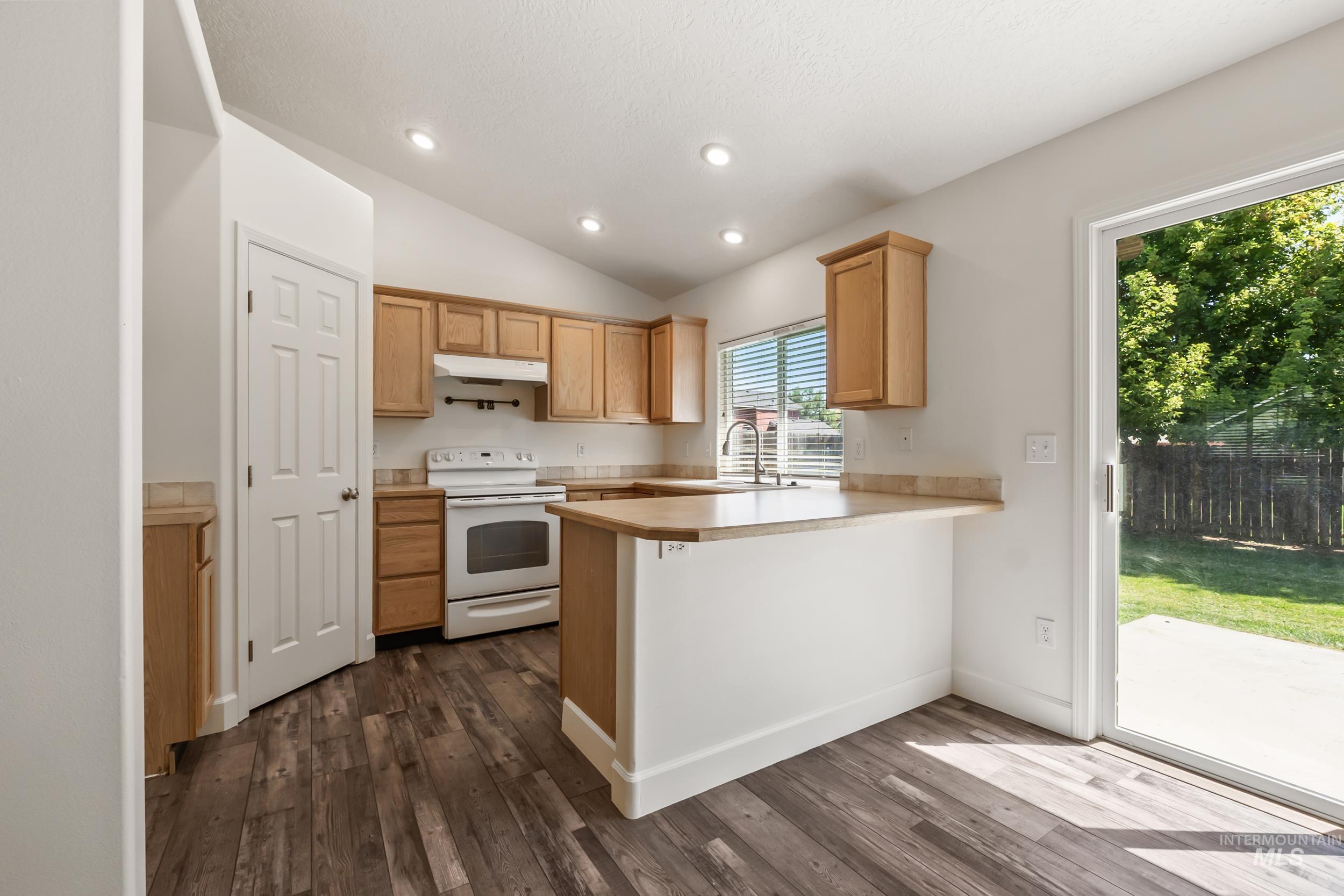 Kitchen with electric range, a peninsula, light countertops, dark wood-style floors, and lofted ceiling