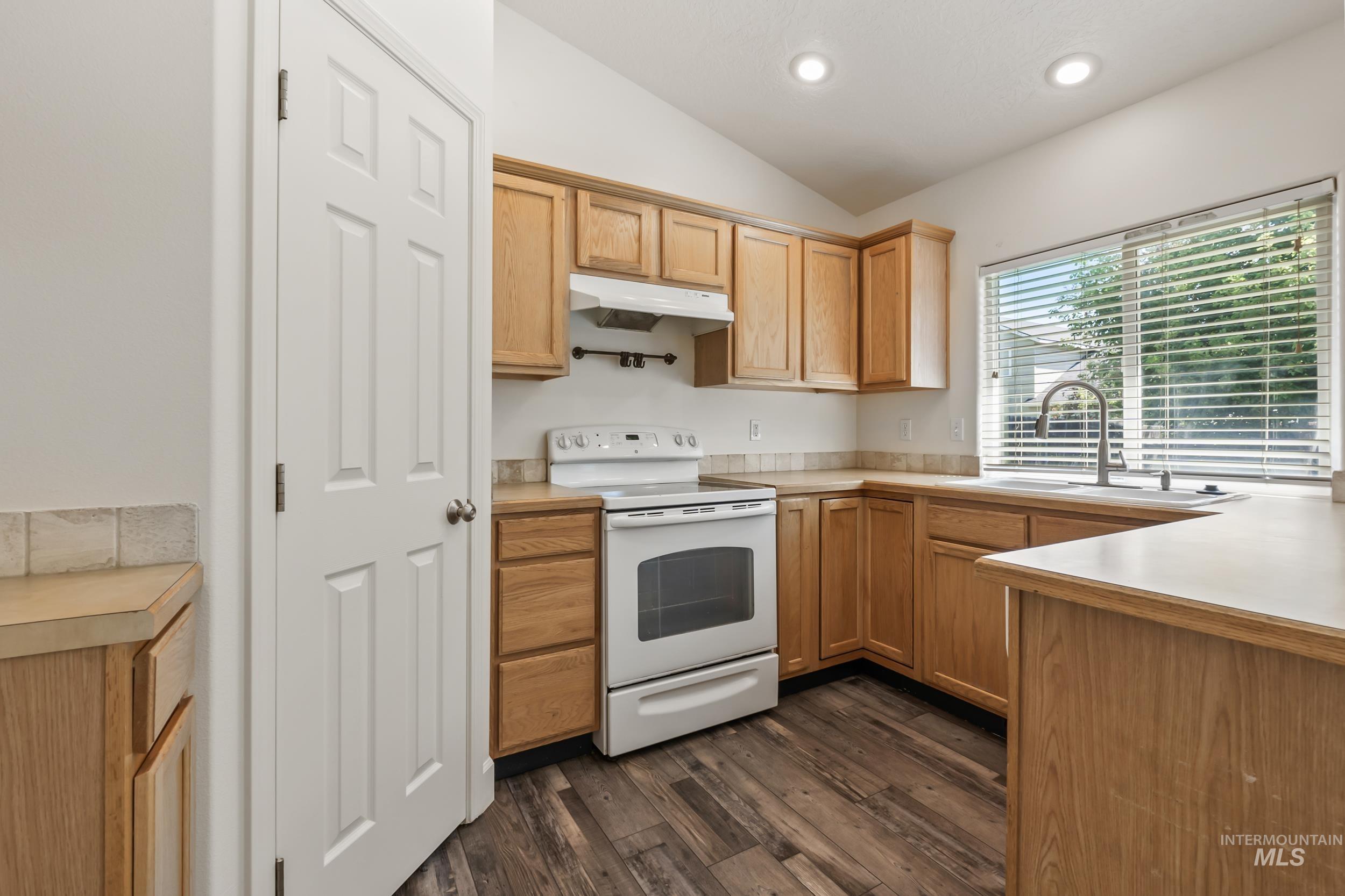 Kitchen featuring white electric range, light countertops, dark wood finished floors, under cabinet range hood, and vaulted ceiling