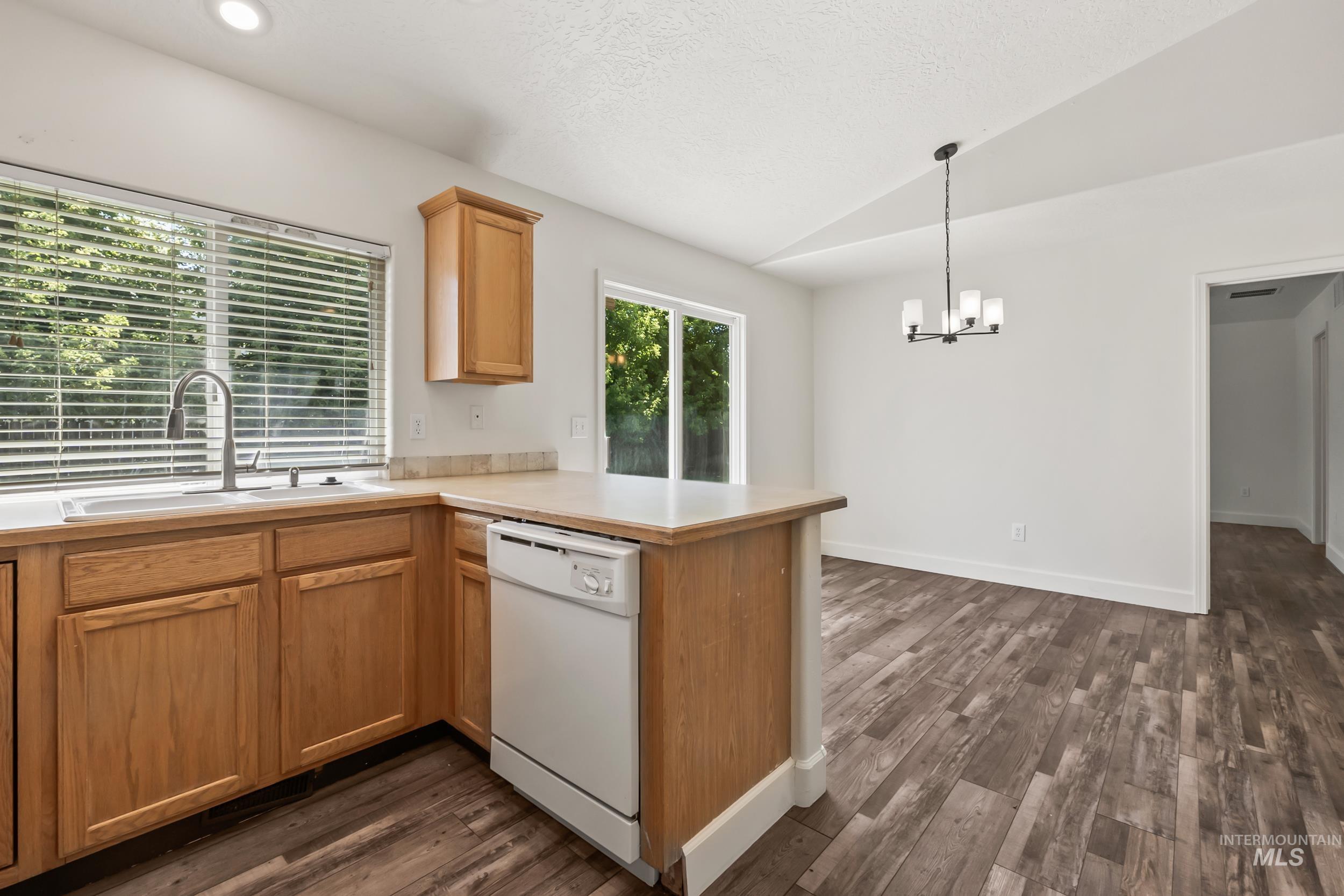 Kitchen featuring light countertops, vaulted ceiling, dishwasher, a peninsula, and dark wood-style flooring