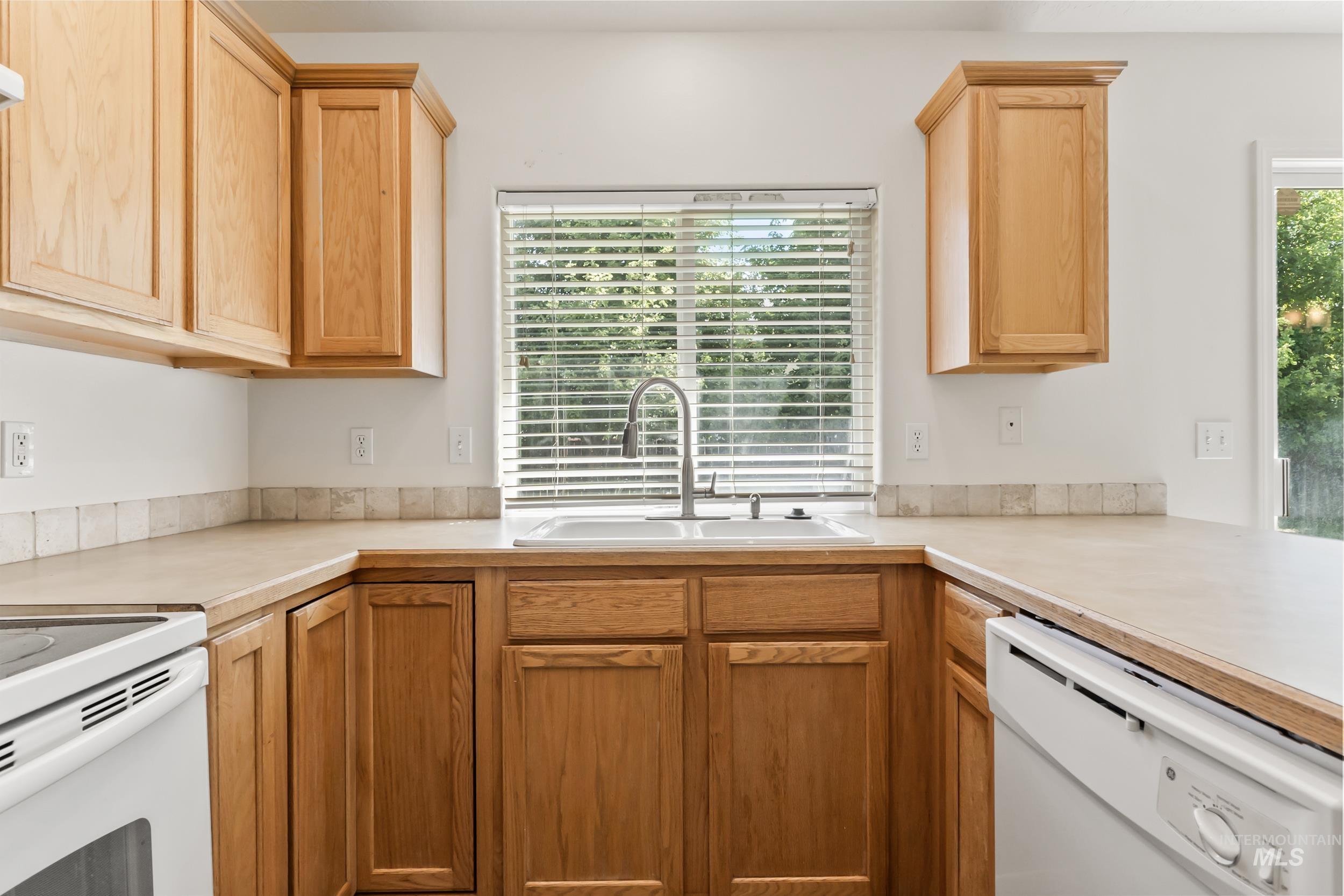 Kitchen with light countertops, white appliances, and light brown cabinets