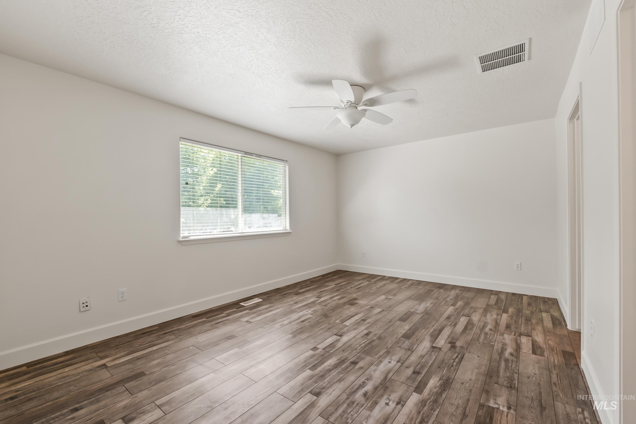 Empty room with dark wood finished floors, a textured ceiling, and a ceiling fan