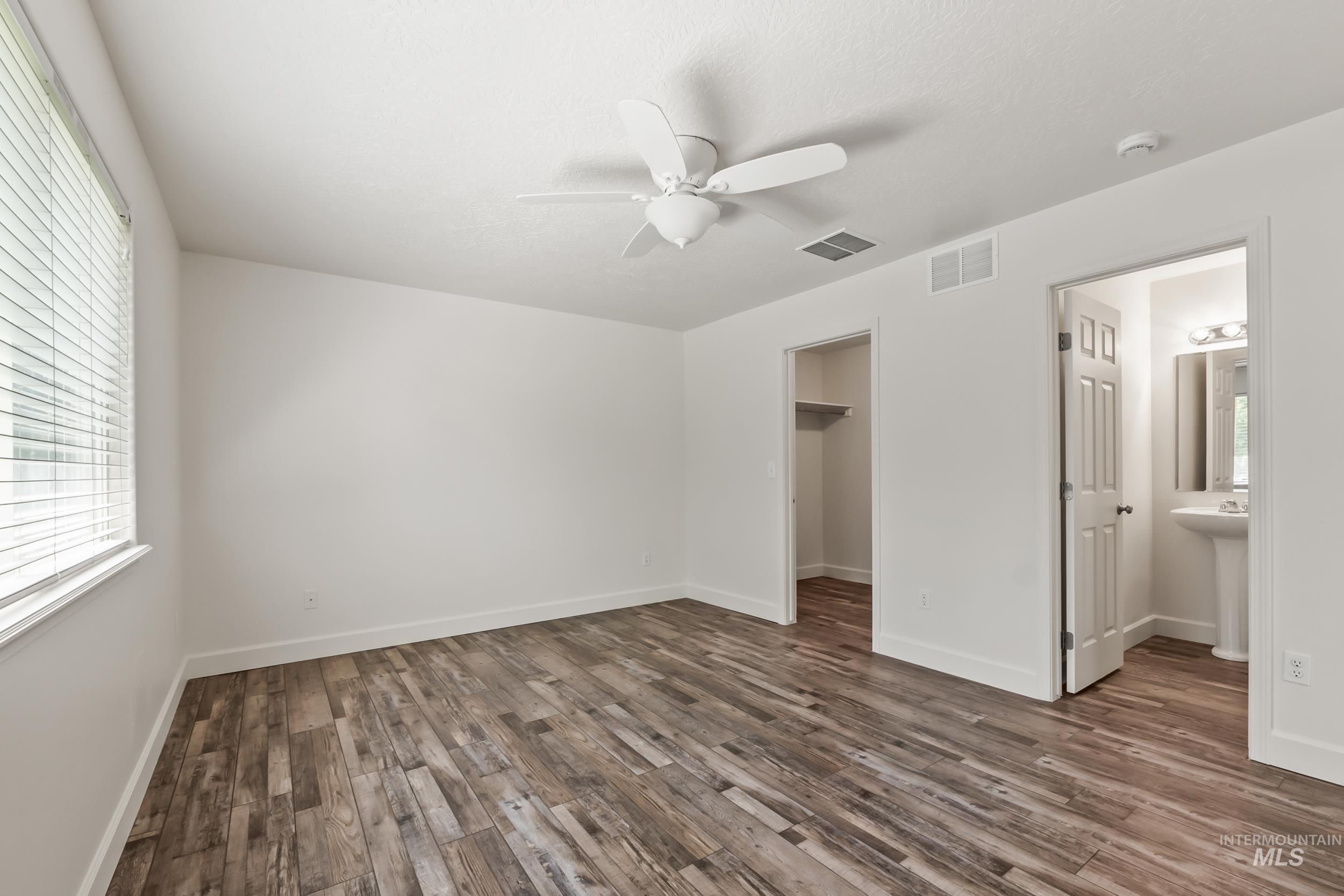Unfurnished bedroom with multiple windows, a walk in closet, and dark wood finished floors