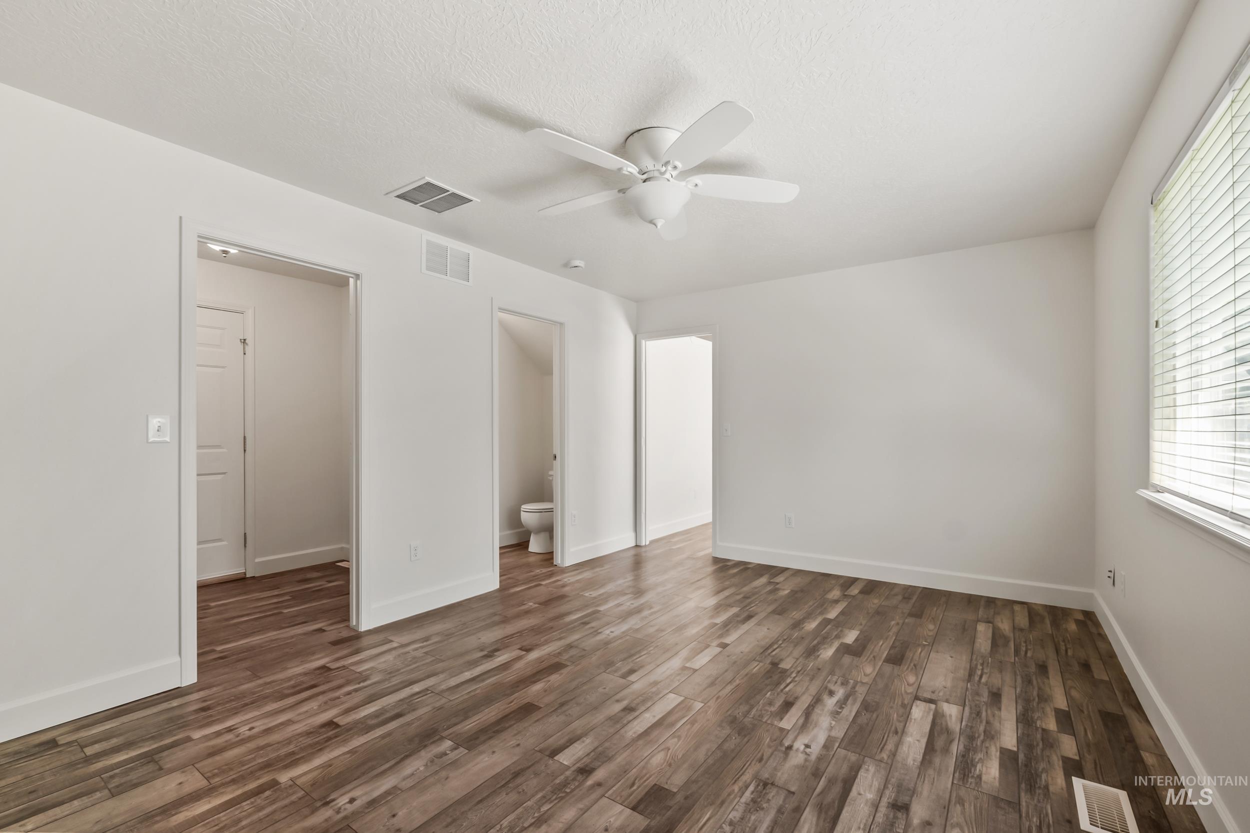 Unfurnished bedroom with ceiling fan, dark wood-type flooring, ensuite bath, and a textured ceiling
