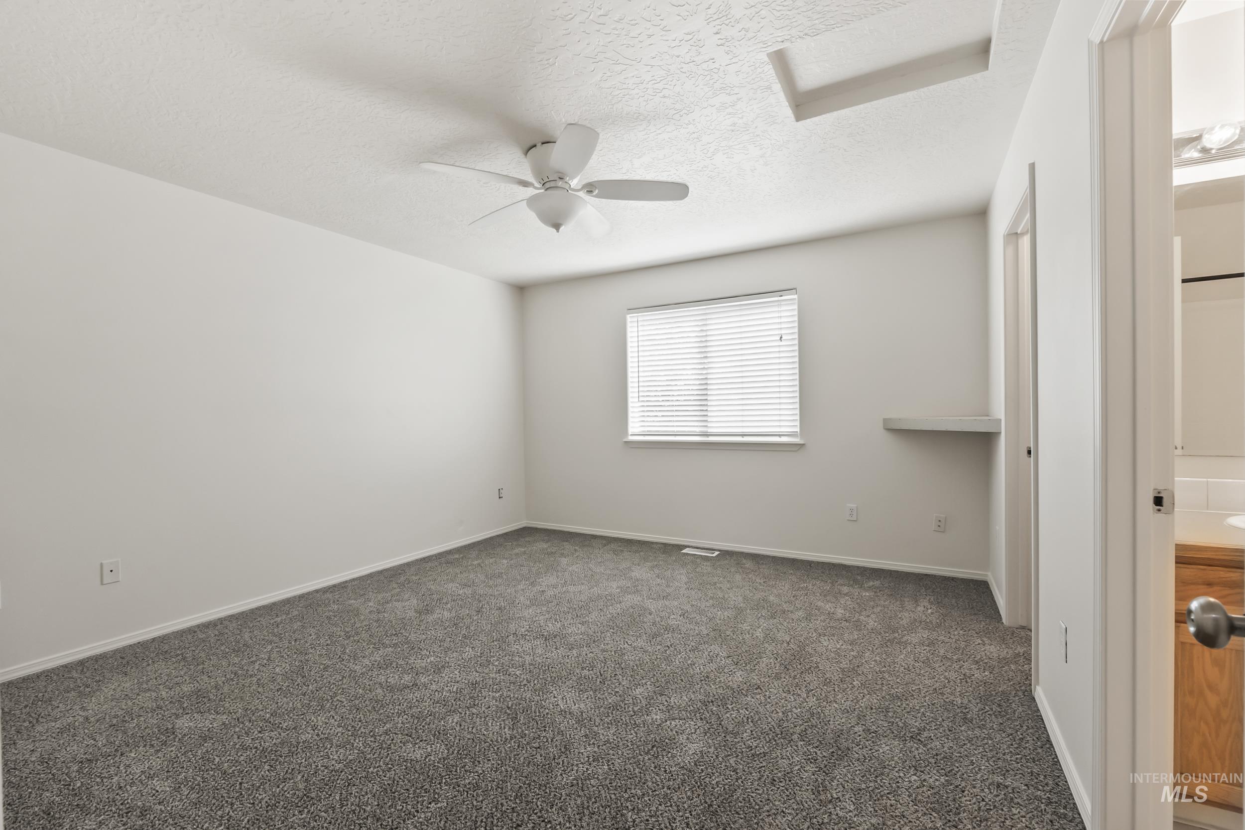 Unfurnished bedroom featuring dark colored carpet, a textured ceiling, and a ceiling fan
