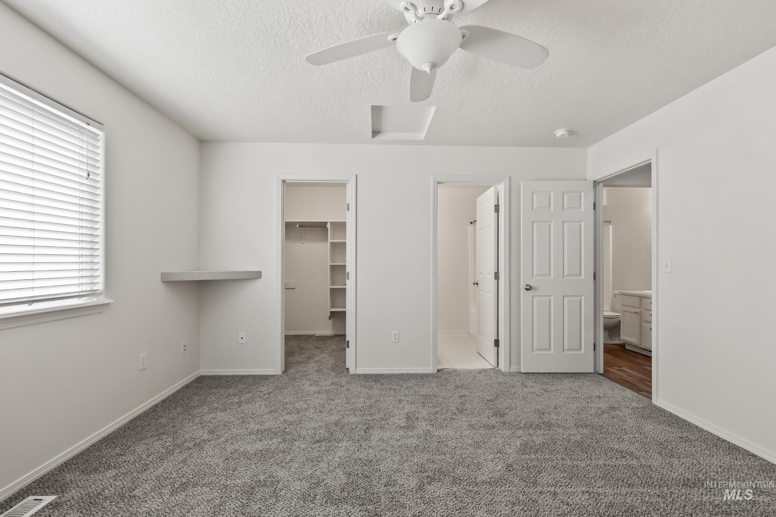 Unfurnished bedroom featuring a textured ceiling, carpet floors, a walk in closet, ceiling fan, and ensuite bathroom