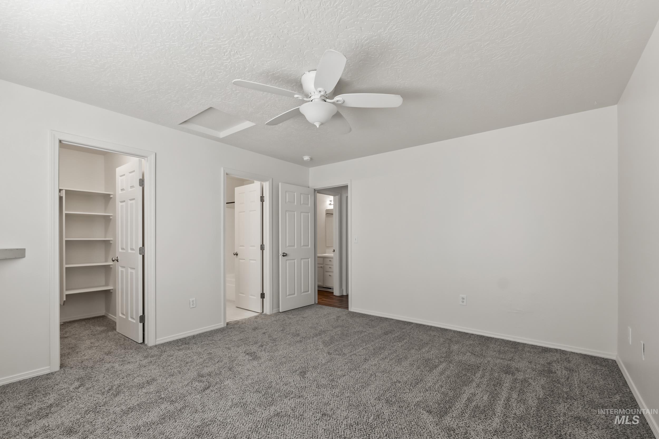 Unfurnished bedroom with a walk in closet, carpet floors, a textured ceiling, ceiling fan, and connected bathroom