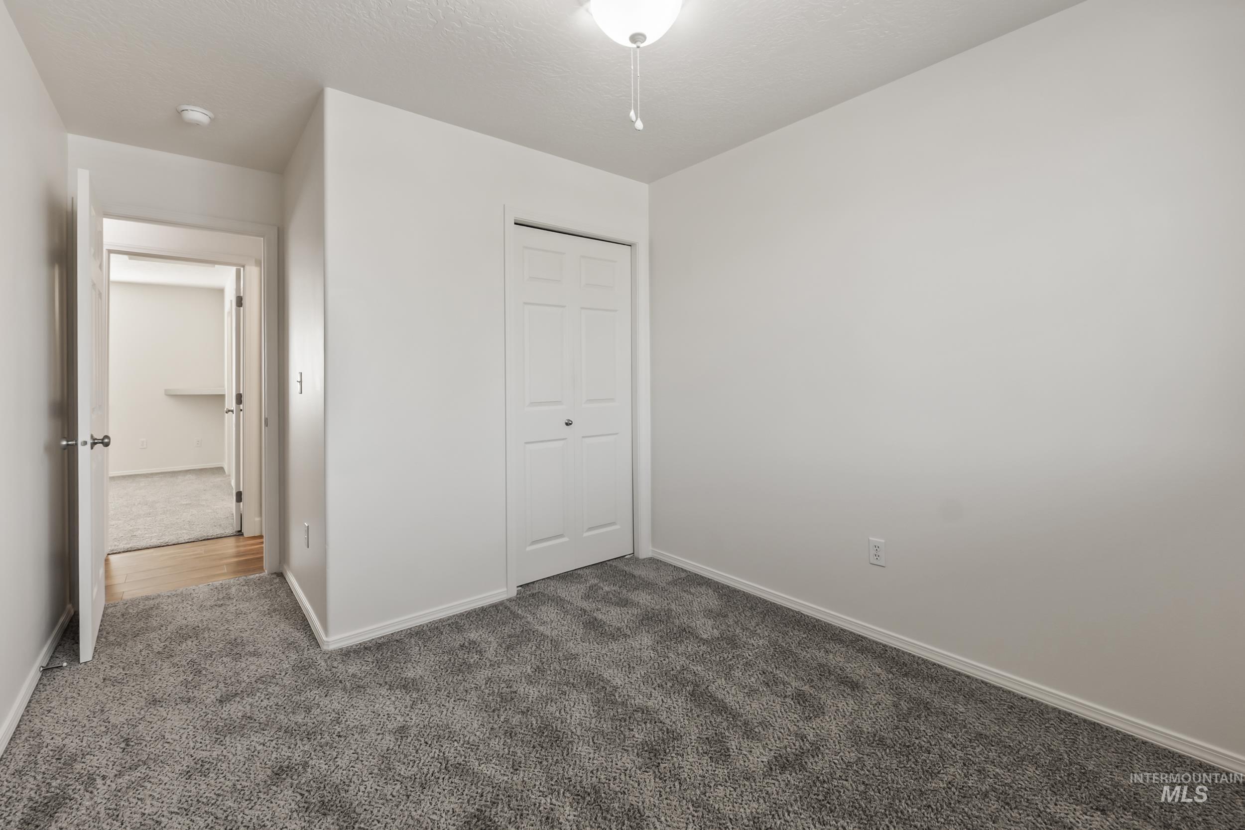 Unfurnished bedroom with dark colored carpet, a closet, and a textured ceiling