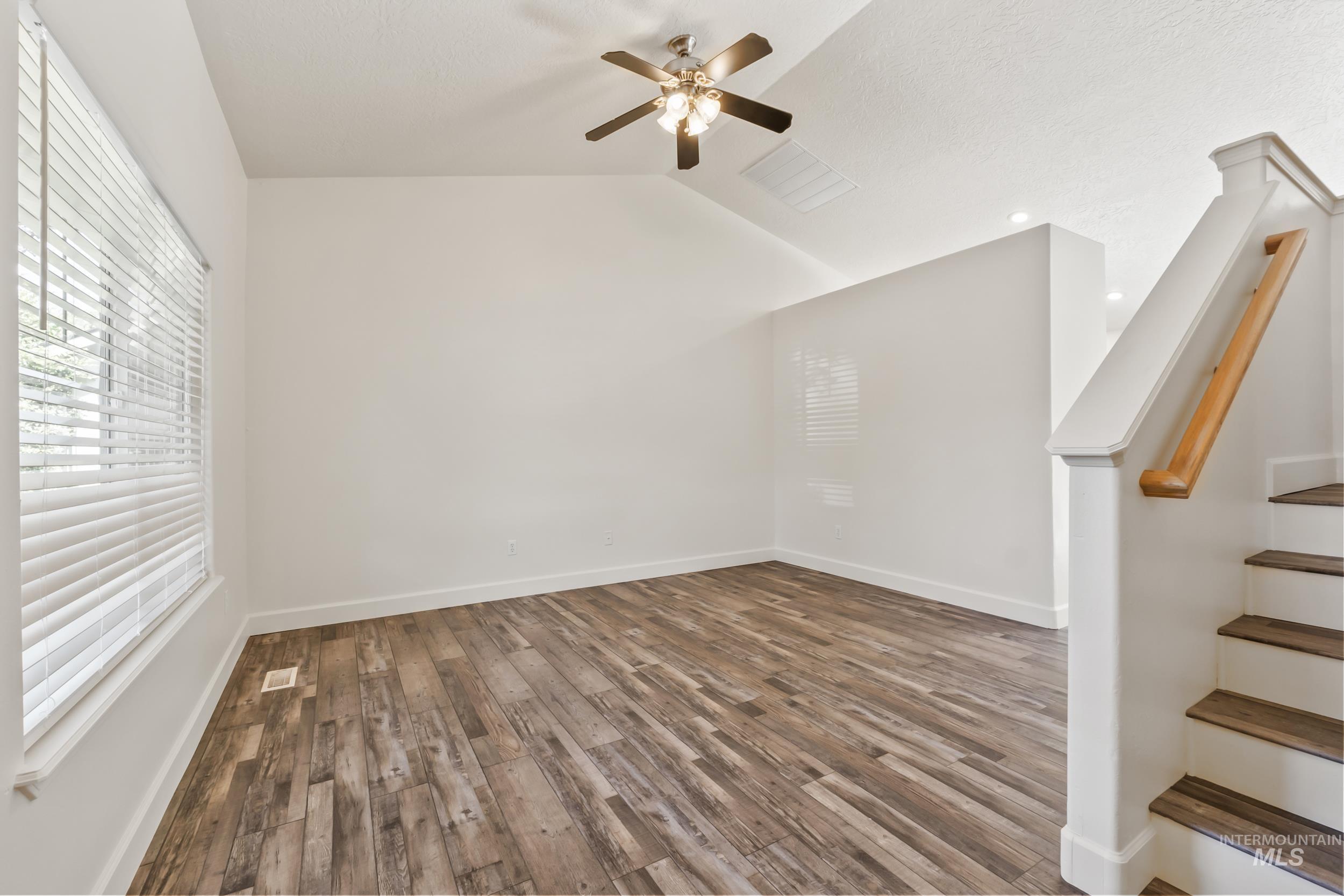 Spare room with stairway, plenty of natural light, wood finished floors, lofted ceiling, and ceiling fan