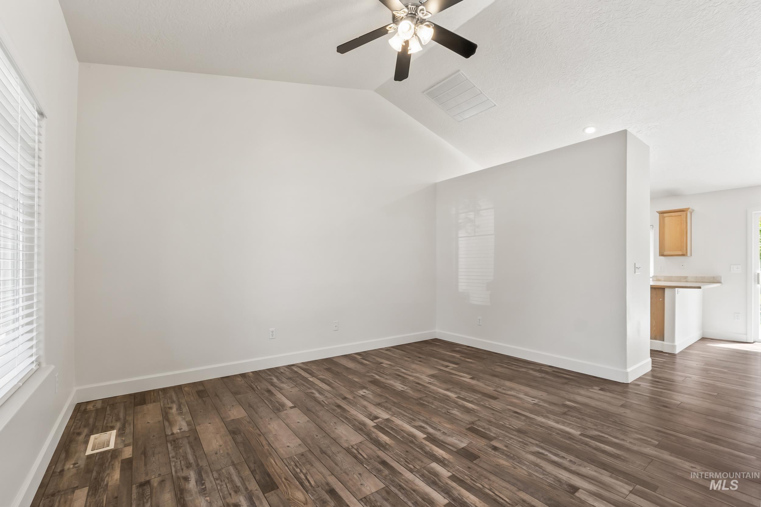 Unfurnished living room with lofted ceiling, dark wood finished floors, a ceiling fan, and a textured ceiling