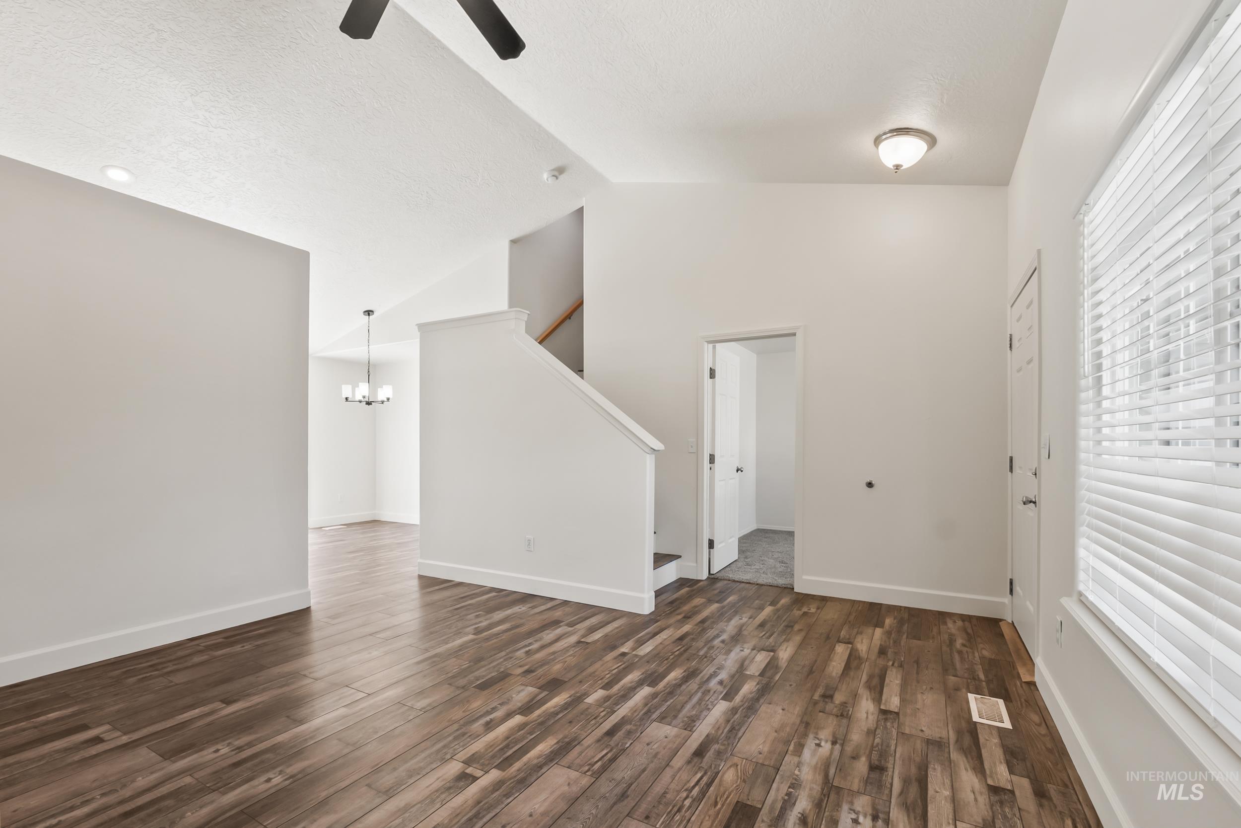 Unfurnished living room featuring dark wood-type flooring, vaulted ceiling, a chandelier, stairs, and a ceiling fan