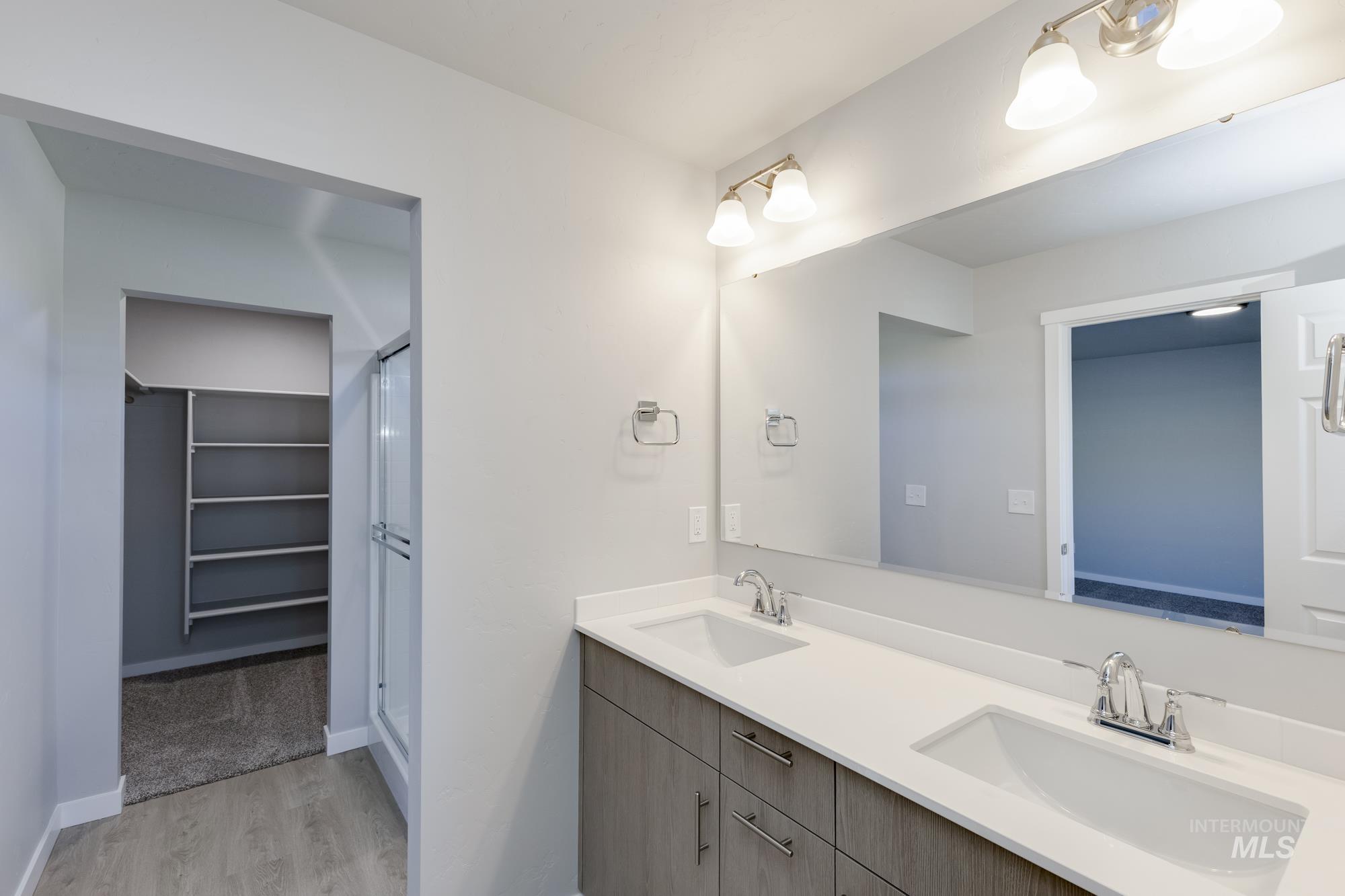 Full bath featuring light wood-style flooring, double vanity, a stall shower, and a walk in closet