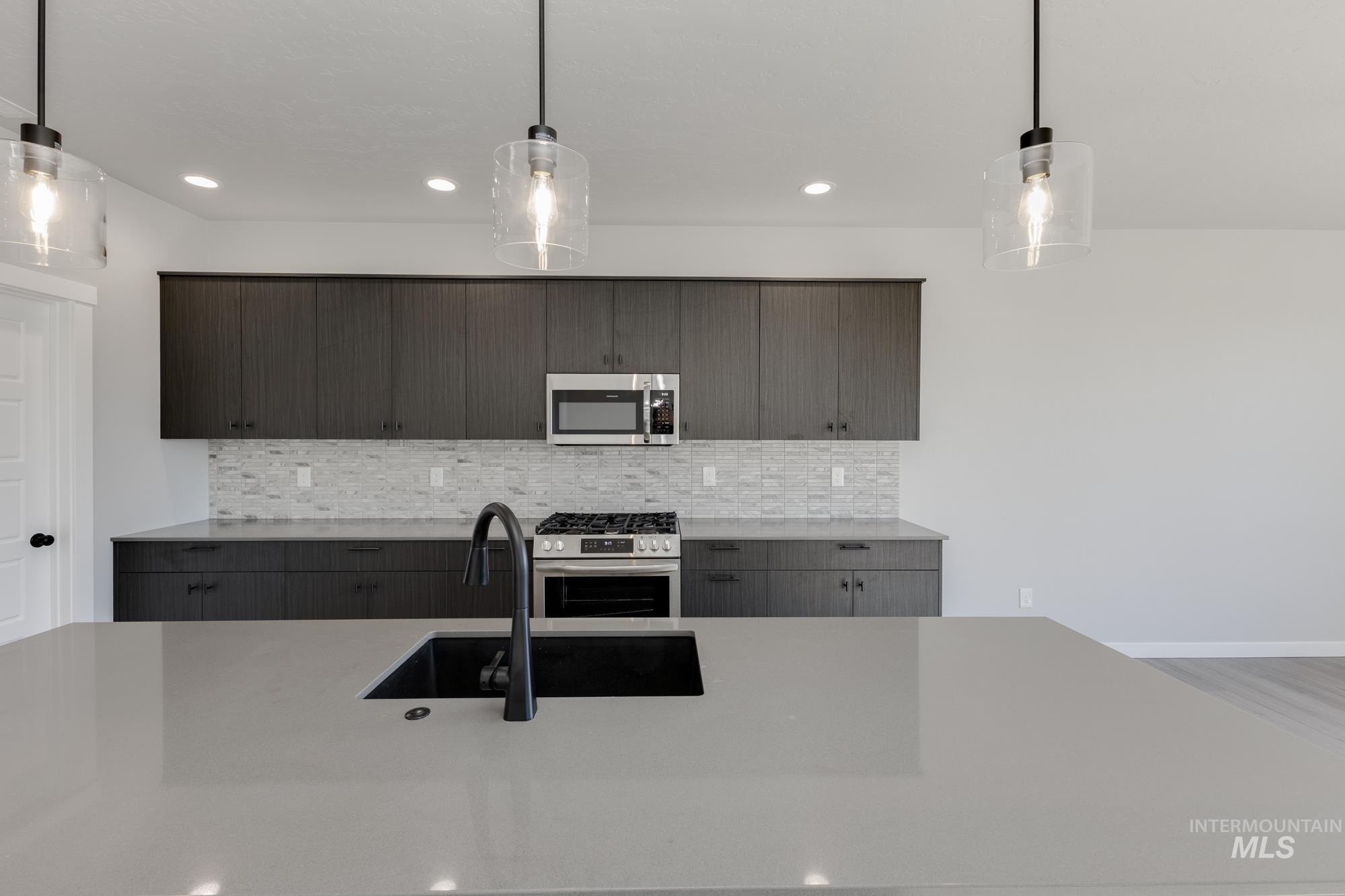 Kitchen featuring decorative light fixtures, appliances with stainless steel finishes, modern cabinets, tasteful backsplash, and light stone countertops