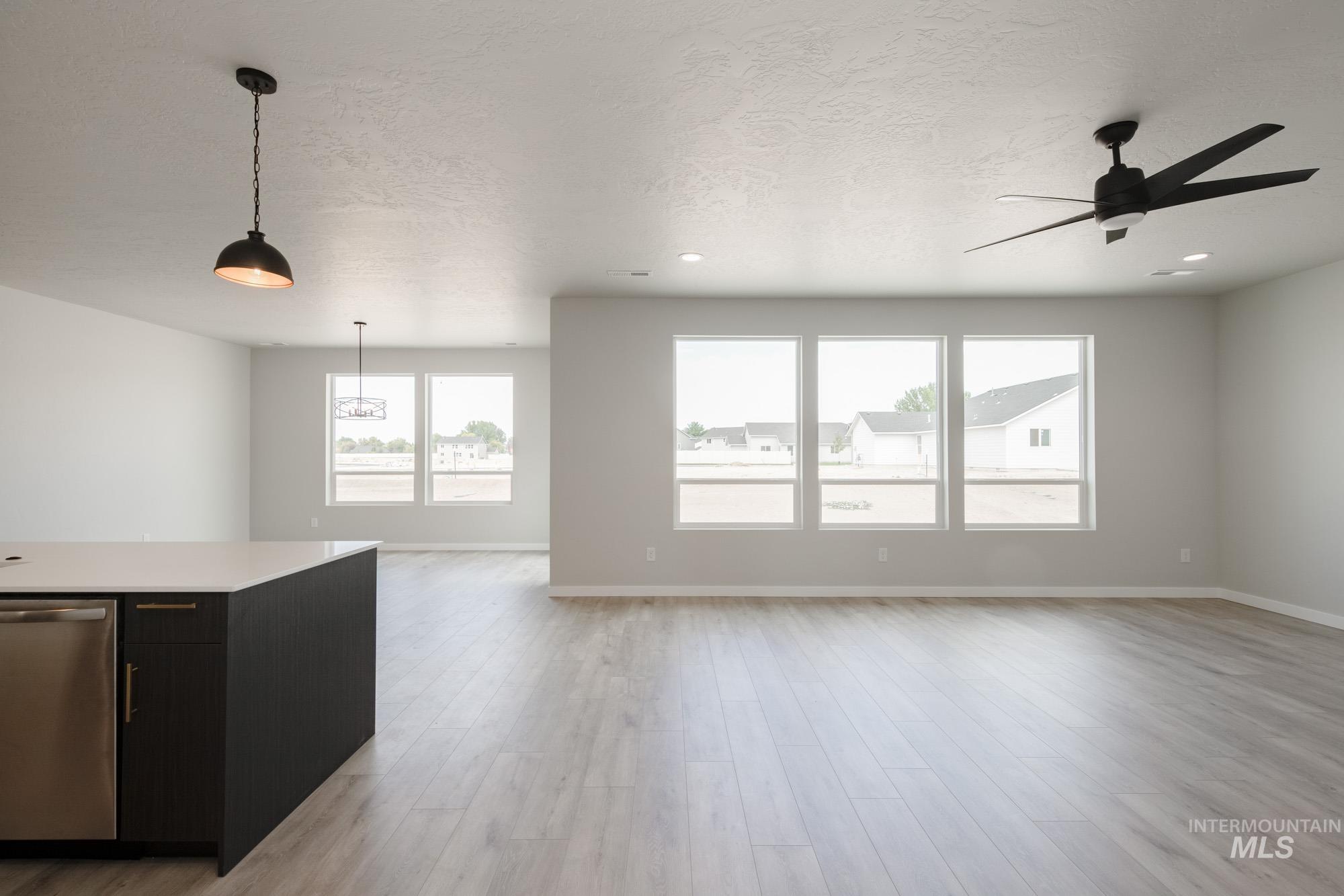 Unfurnished living room with plenty of natural light, light wood finished floors, a textured ceiling, and a ceiling fan