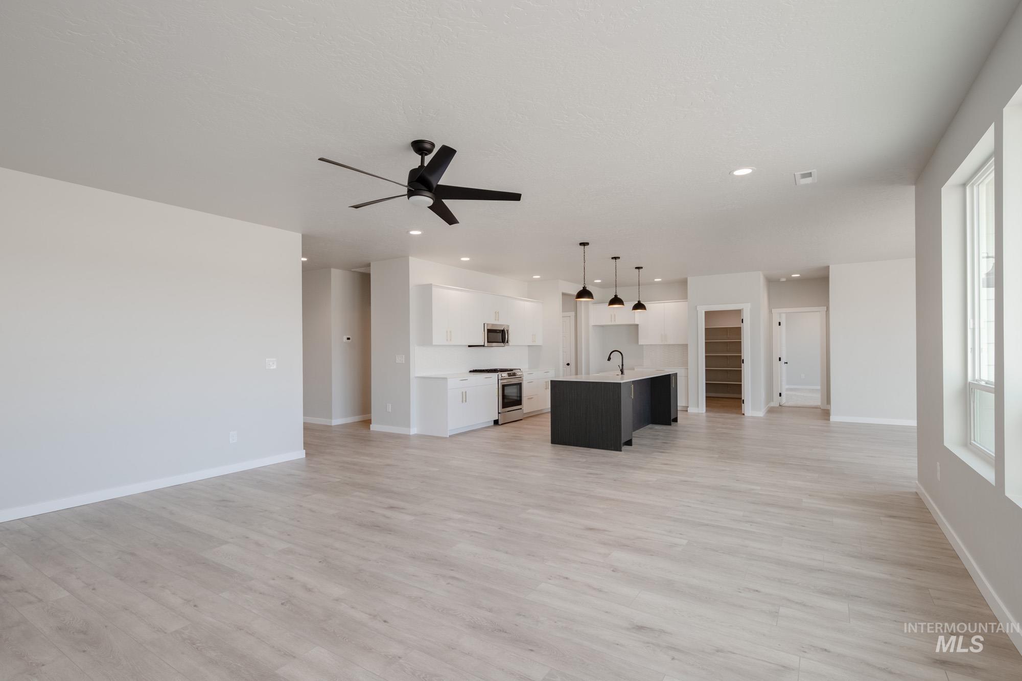 Unfurnished living room featuring light wood-style floors, a ceiling fan, and recessed lighting