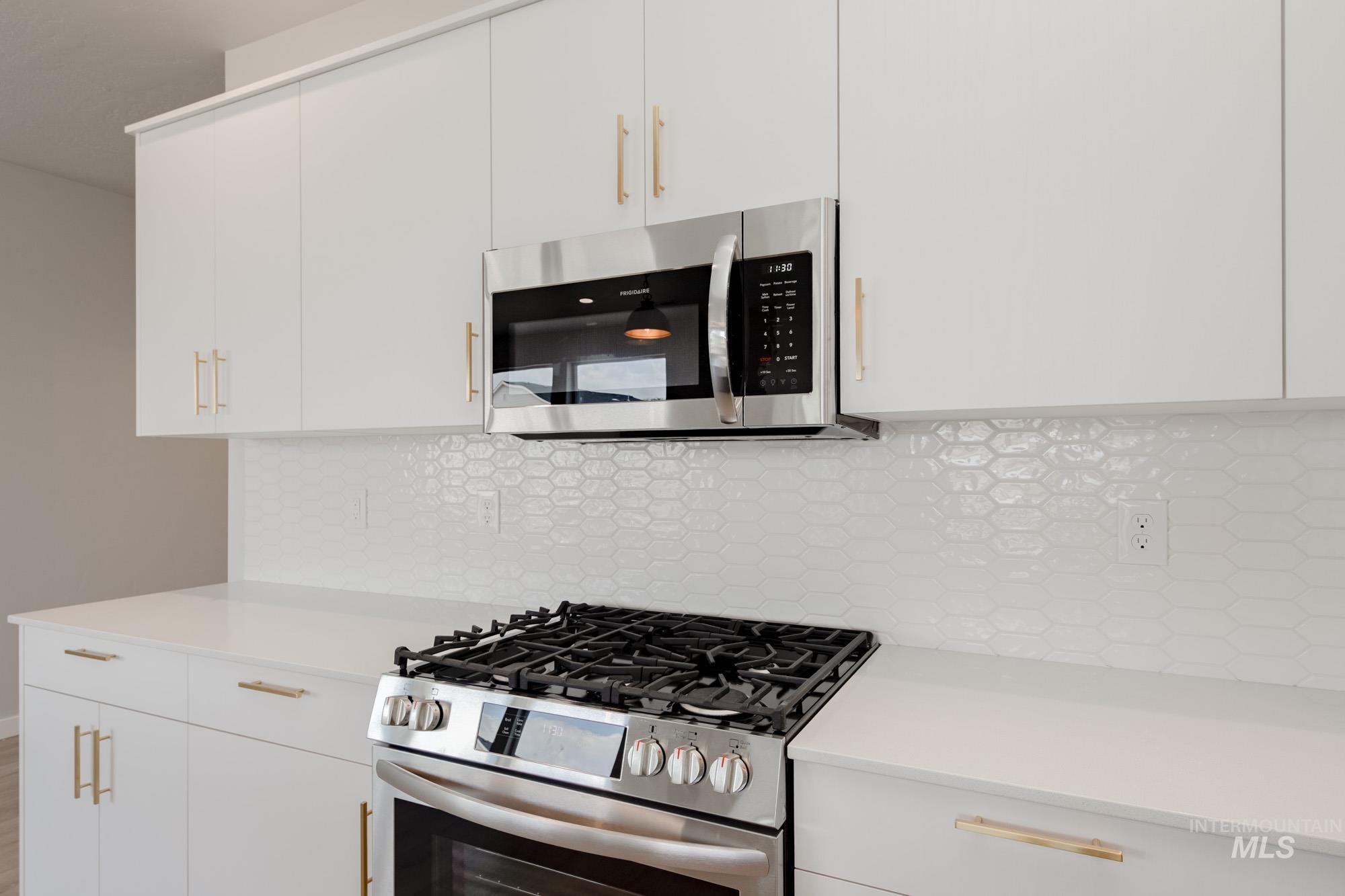 Kitchen with stainless steel appliances, decorative backsplash, and white cabinets