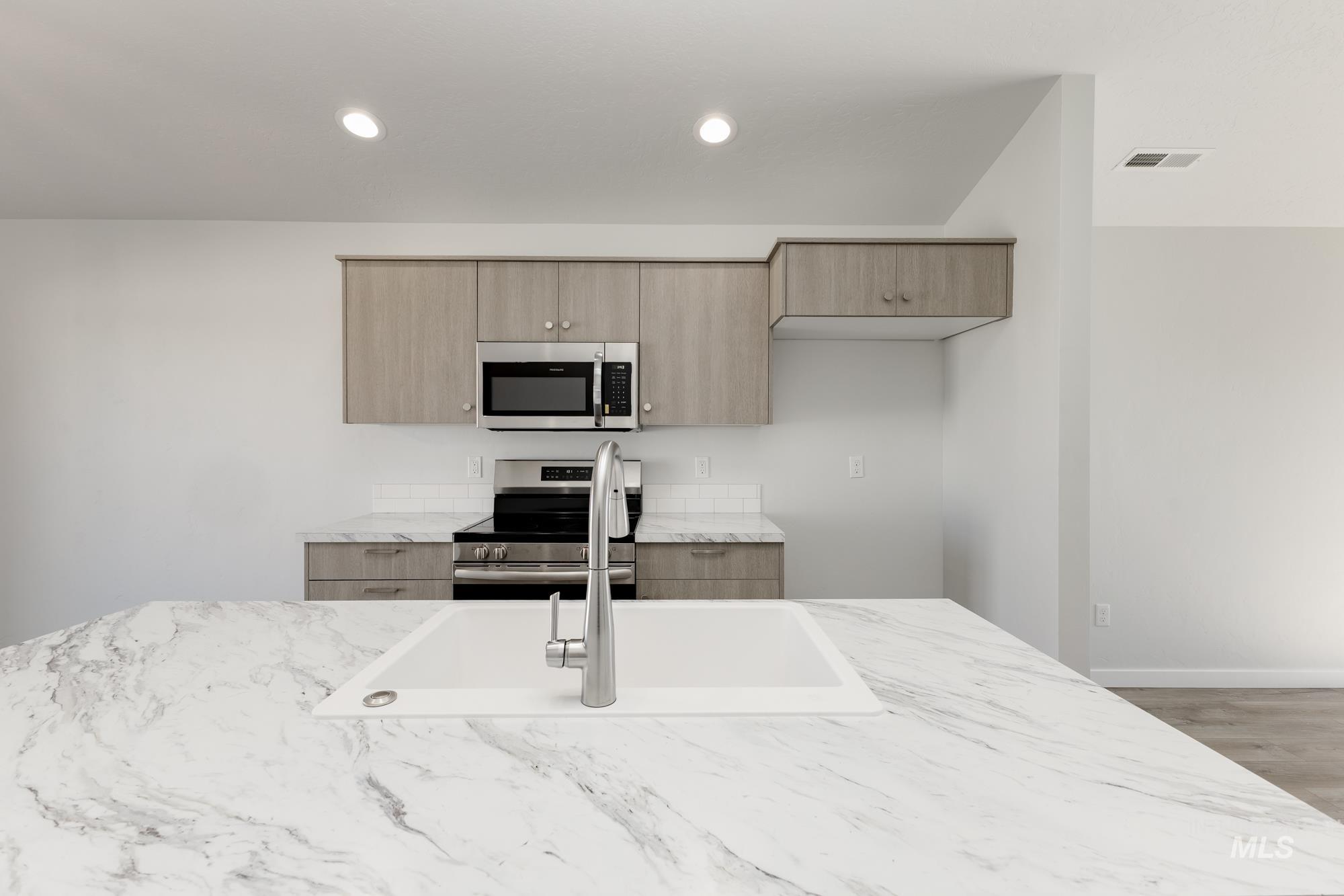 Kitchen featuring light stone counters, modern cabinets, stainless steel appliances, light brown cabinetry, and recessed lighting