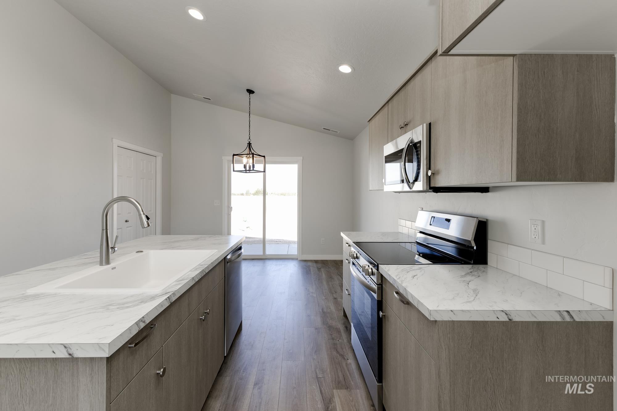 Kitchen featuring stainless steel appliances, modern cabinets, light countertops, vaulted ceiling, and light brown cabinetry