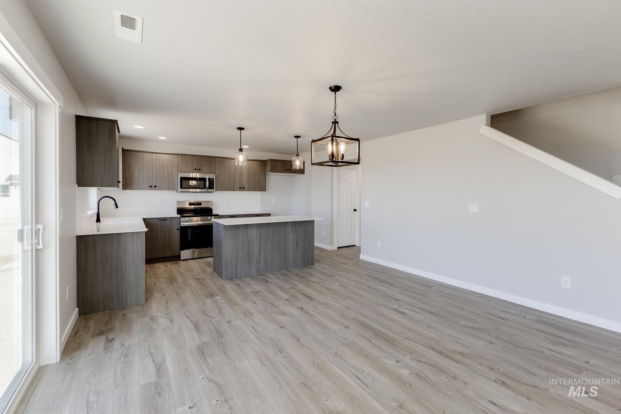 Kitchen with light countertops, a kitchen island, hanging light fixtures, appliances with stainless steel finishes, and a chandelier