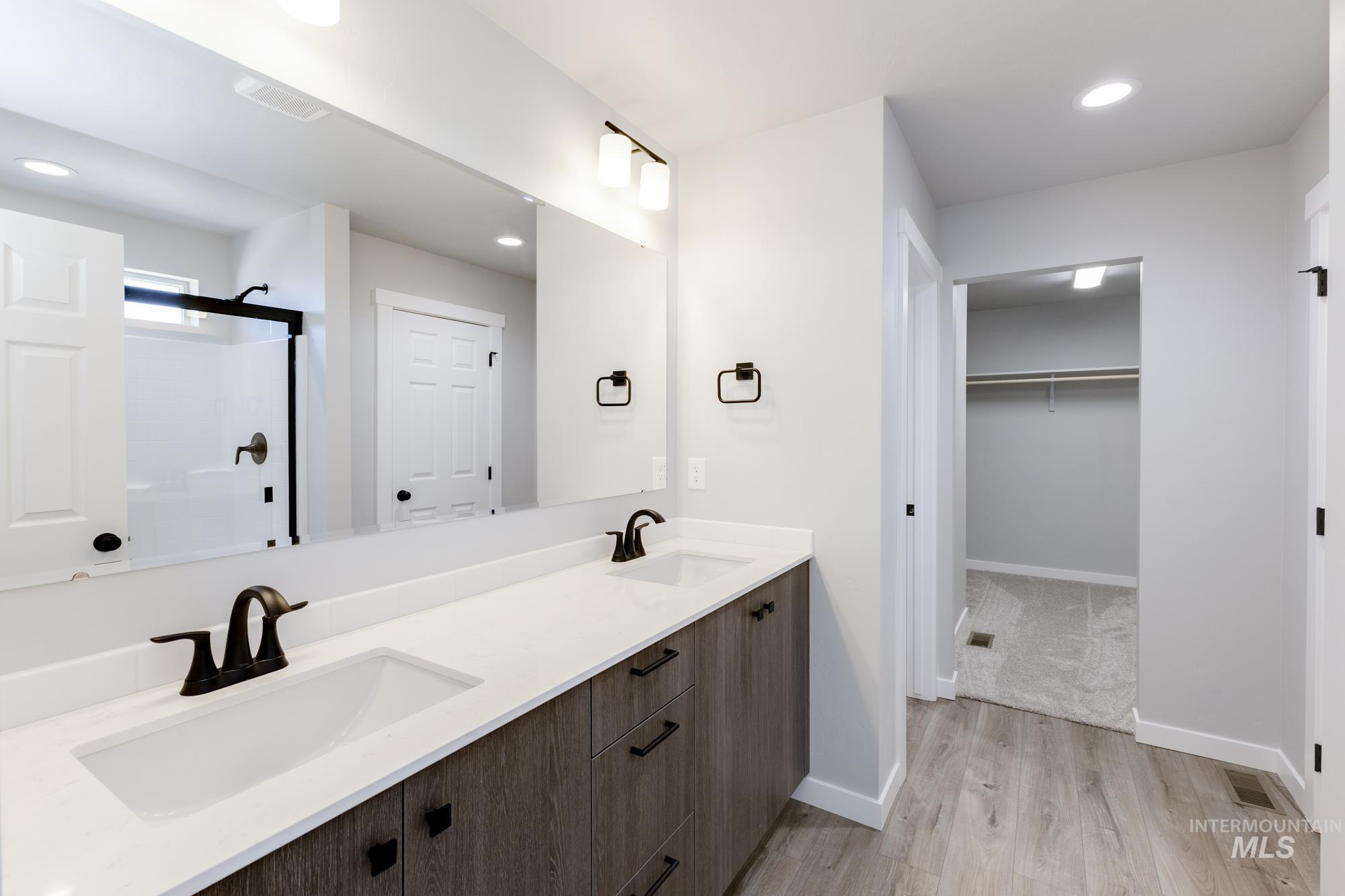 Bathroom with recessed lighting, a shower stall, light wood-style floors, double vanity, and a walk in closet