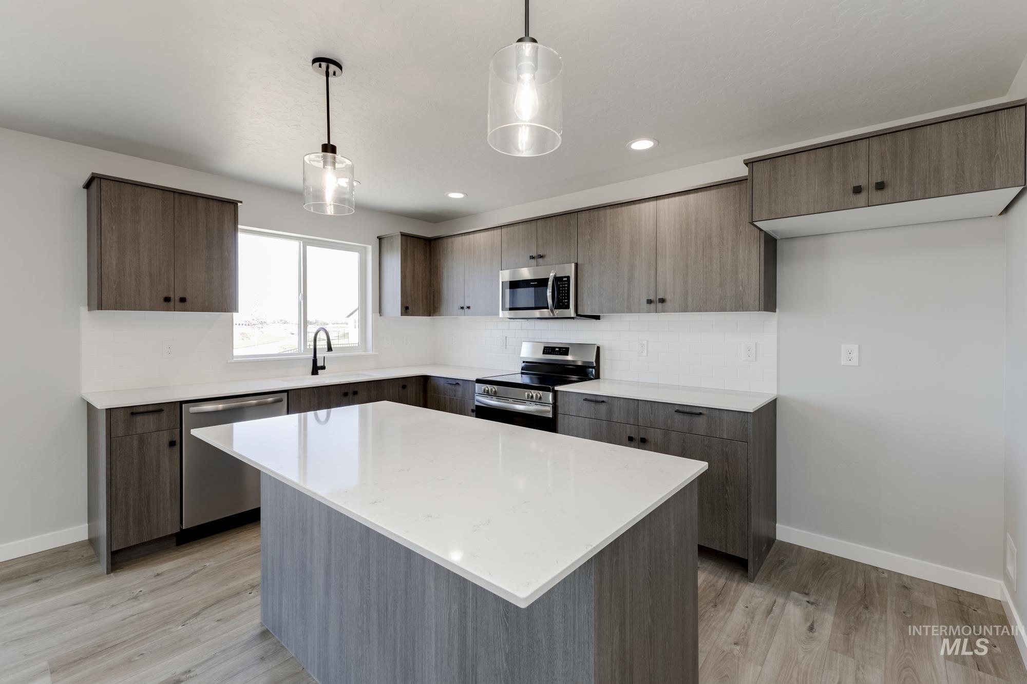 Kitchen featuring decorative light fixtures, tasteful backsplash, appliances with stainless steel finishes, a kitchen island, and light stone counters