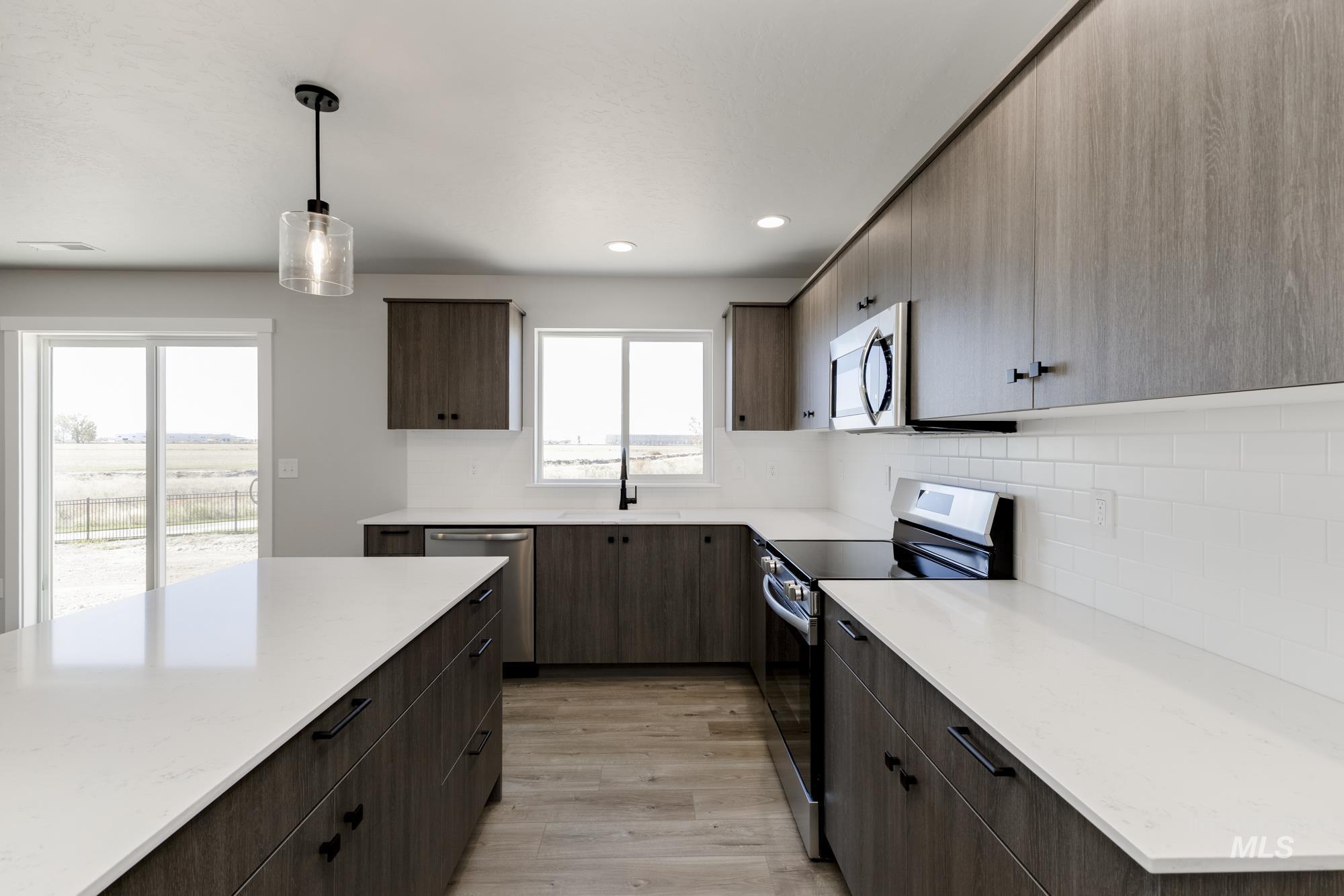 Kitchen with appliances with stainless steel finishes, decorative light fixtures, backsplash, light wood-type flooring, and dark brown cabinets